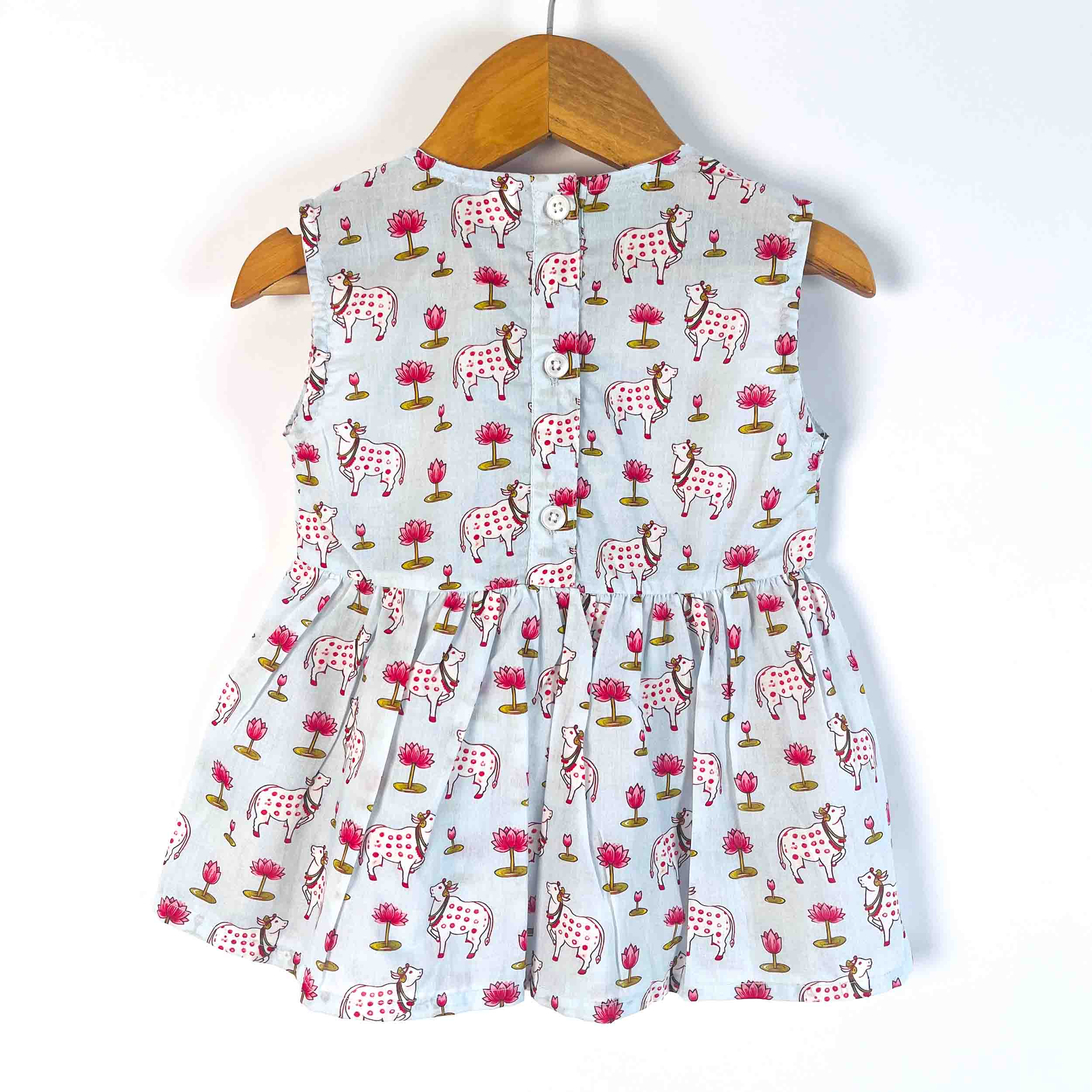Back view of a Blue Pichwai cotton sleeveless dress with button-back closure, flared design, and all-over cow and floral print for girls