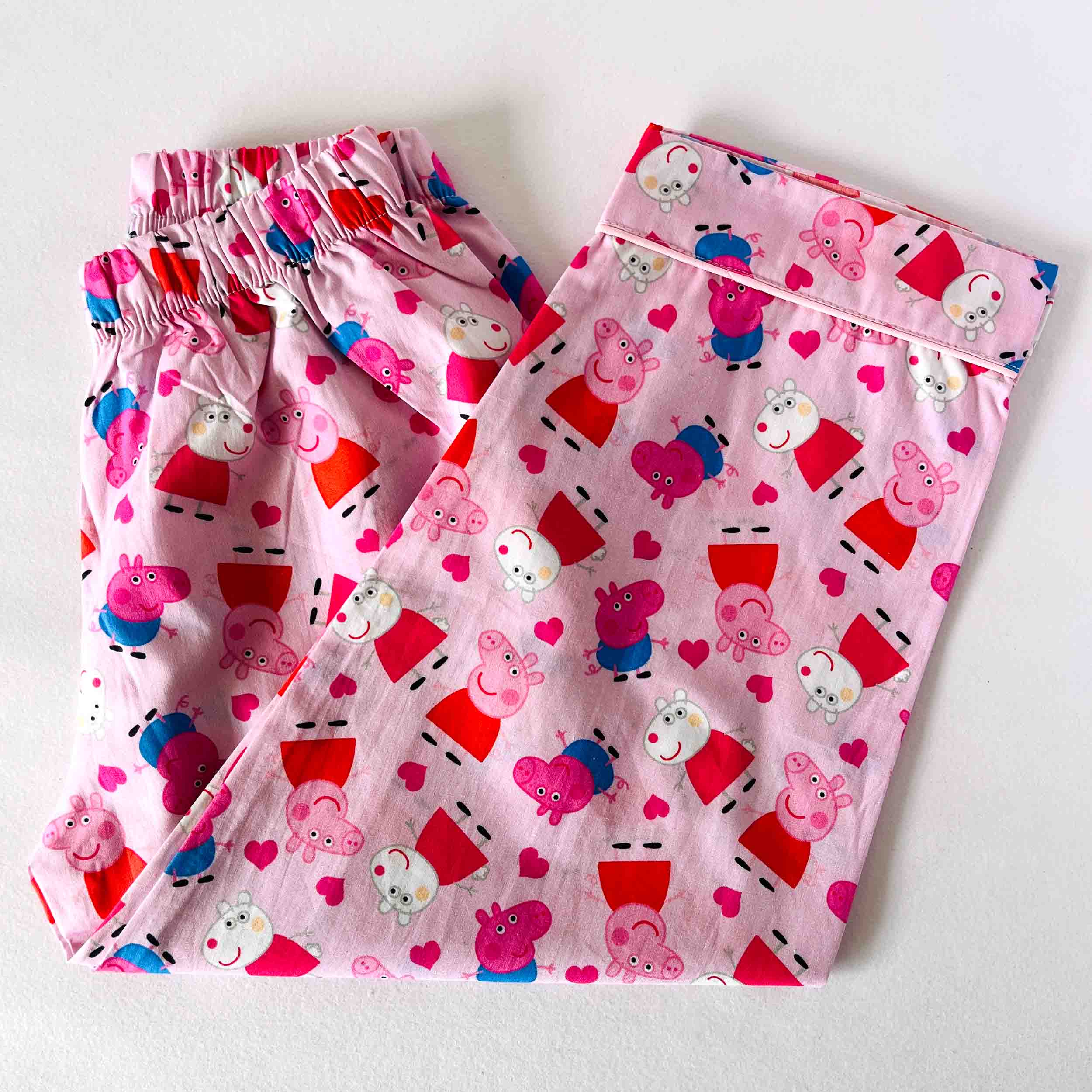 Pink children's pajama set with peppa pig cartoon character pattern on a white background
