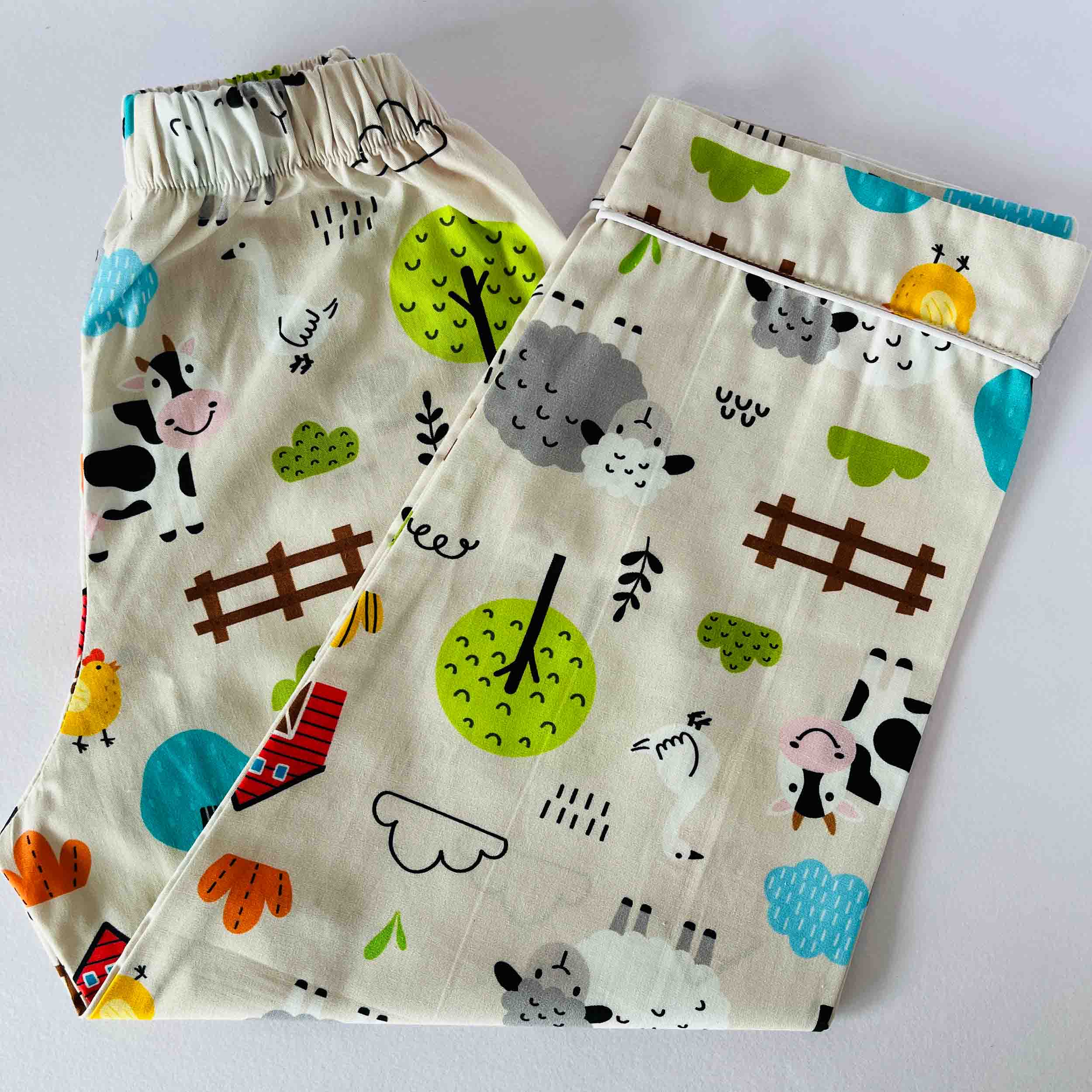 Two pairs of children's pants with farm animal and nature-themed prints on a white background.
