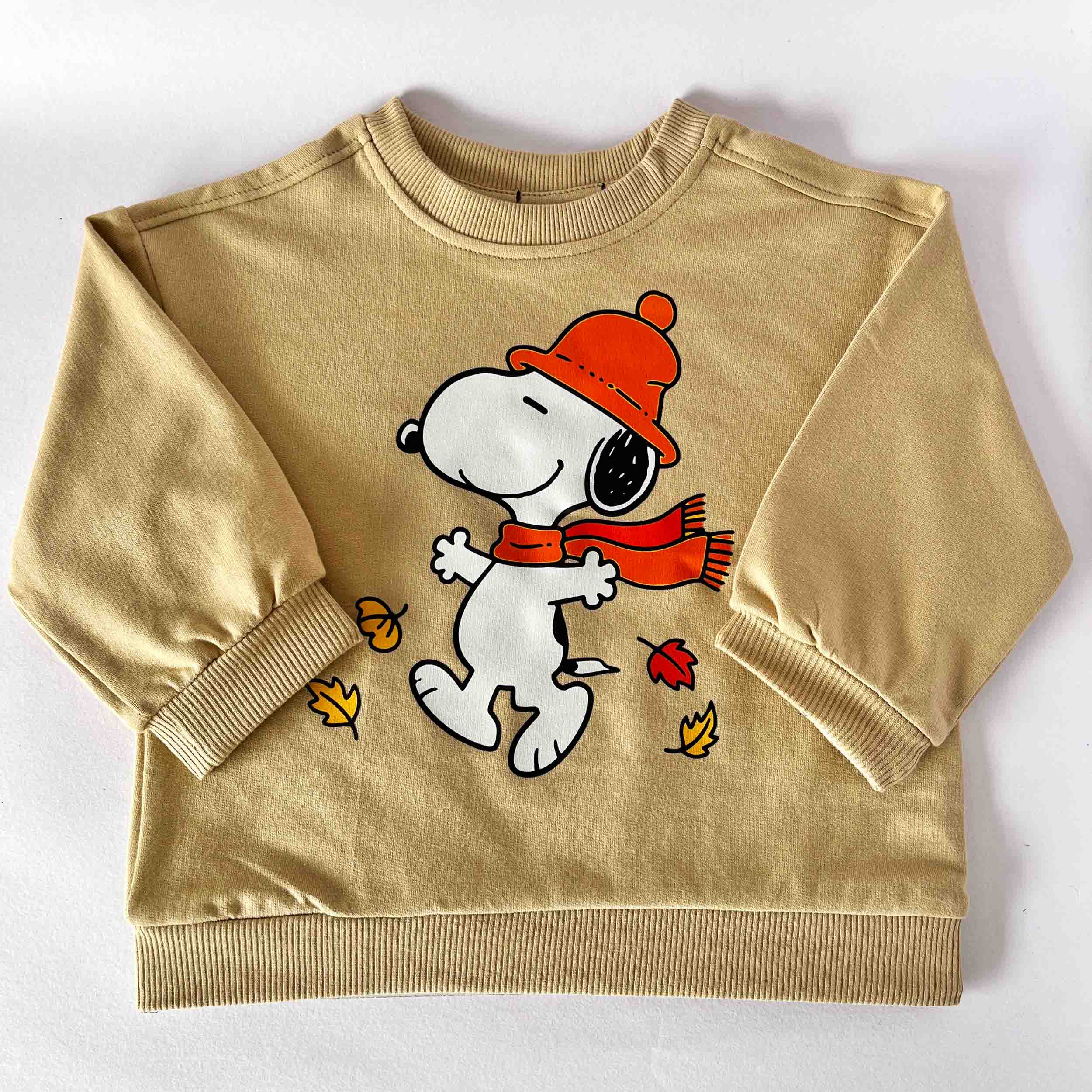 Beige sweatshirt with cartoon dog wearing an orange hat and scarf on a white background