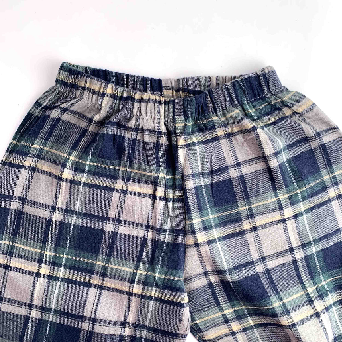 A close-up of a pair of plaid lounge pants or pajama shorts with an elastic waistband, featuring a pattern of navy blue, gray, beige, and green.