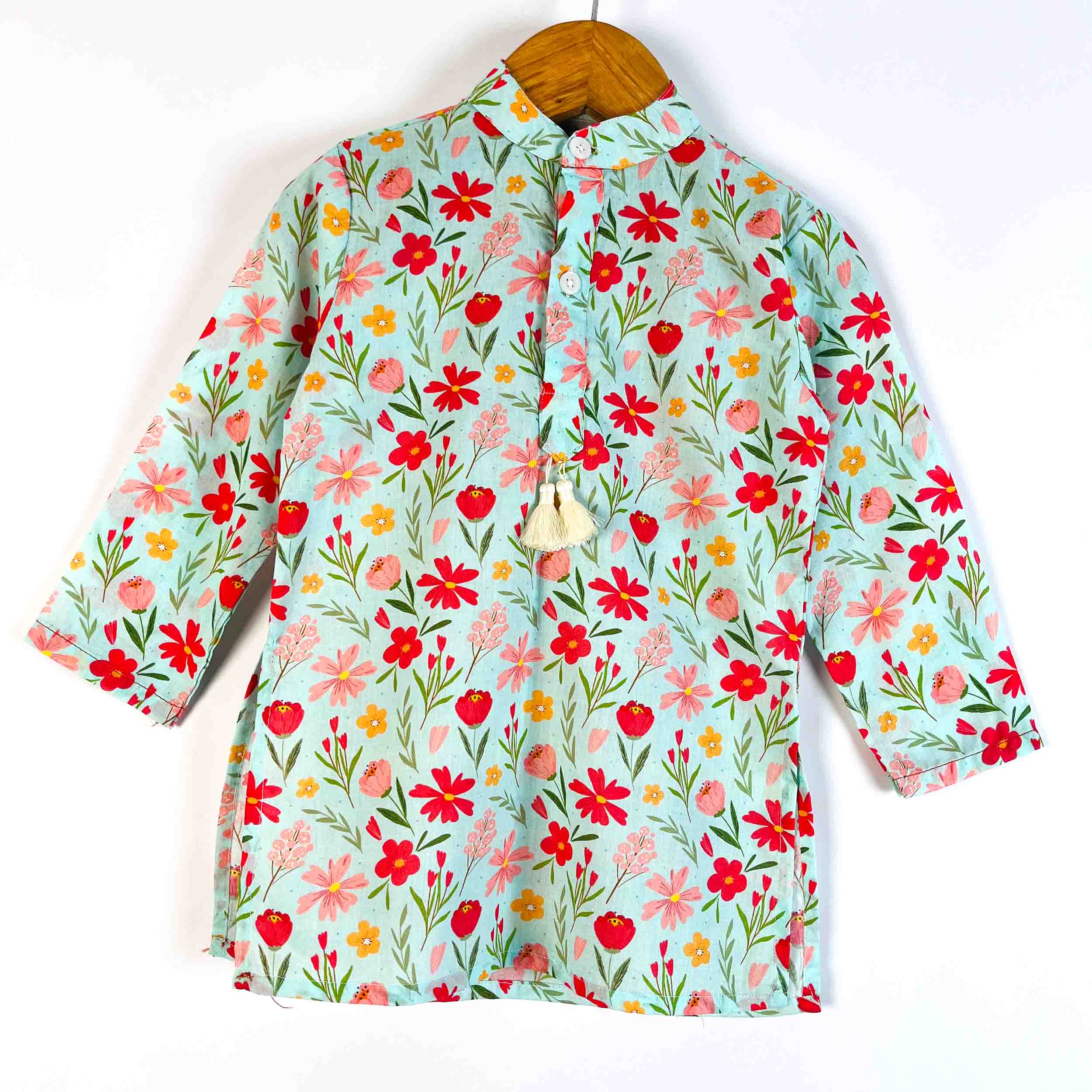 A long-sleeve button-up shirt with a colorful floral print on a light mint green background, hanging on a wooden hanger against a plain white wall.