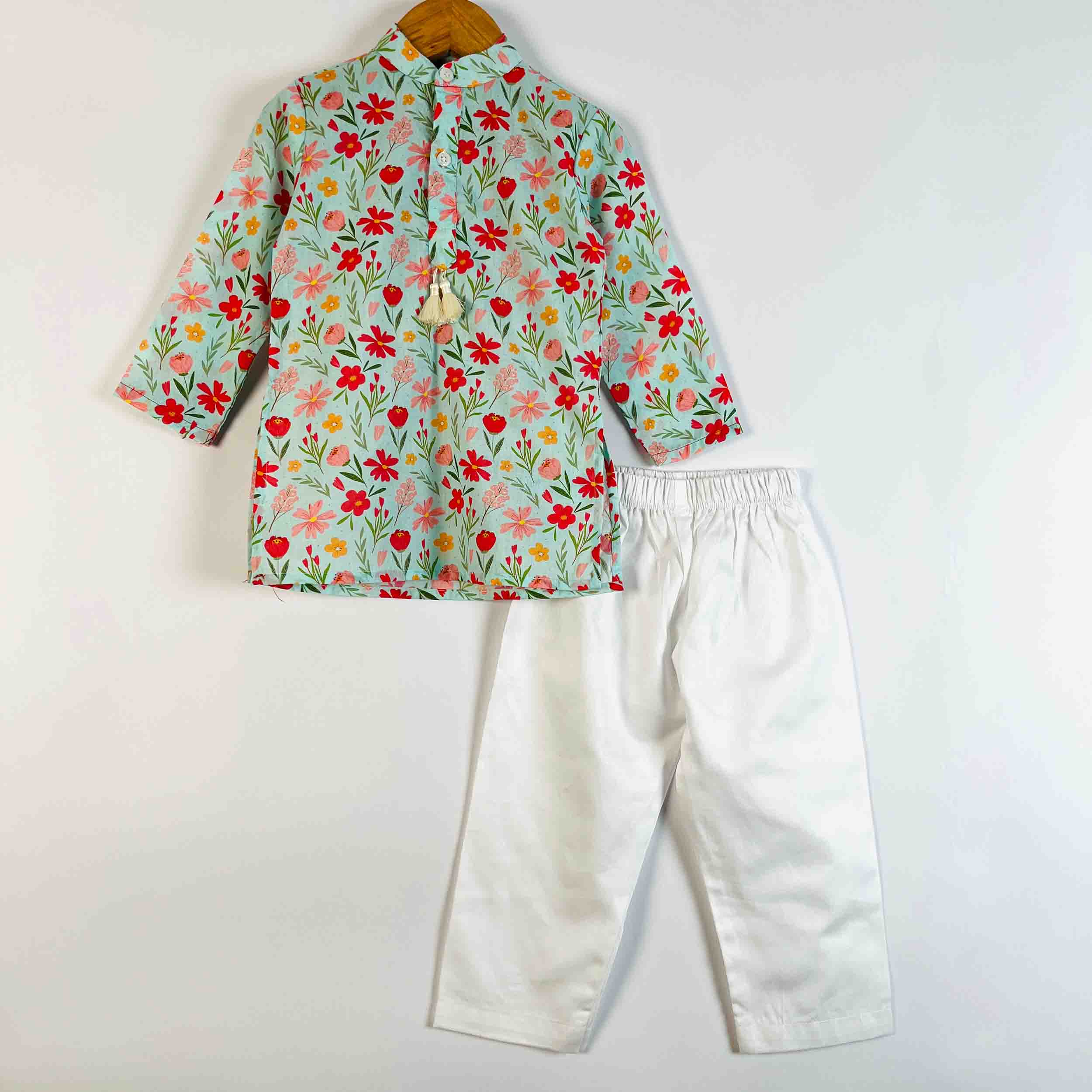 A children's two-piece outfit set featuring a long-sleeve button-up shirt with a colorful floral print on a mint green background, paired with white pants, displayed on a wooden hanger against a plain white wall.