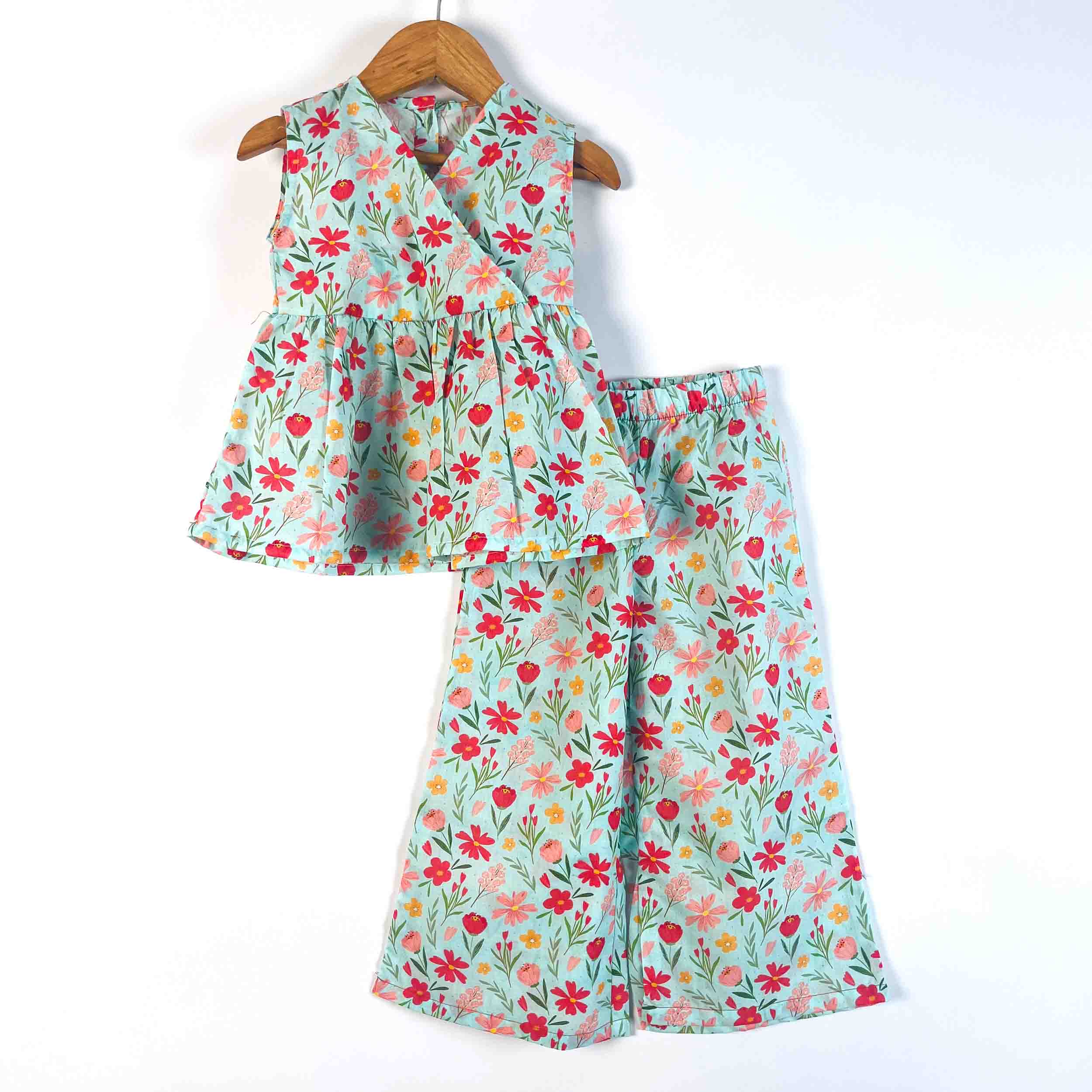 A two-piece girls' outfit set featuring a sleeveless peplum top and matching wide-leg pants, both in a light mint green floral print with red, pink, and yellow flowers, hanging on a wooden hanger against a white background.