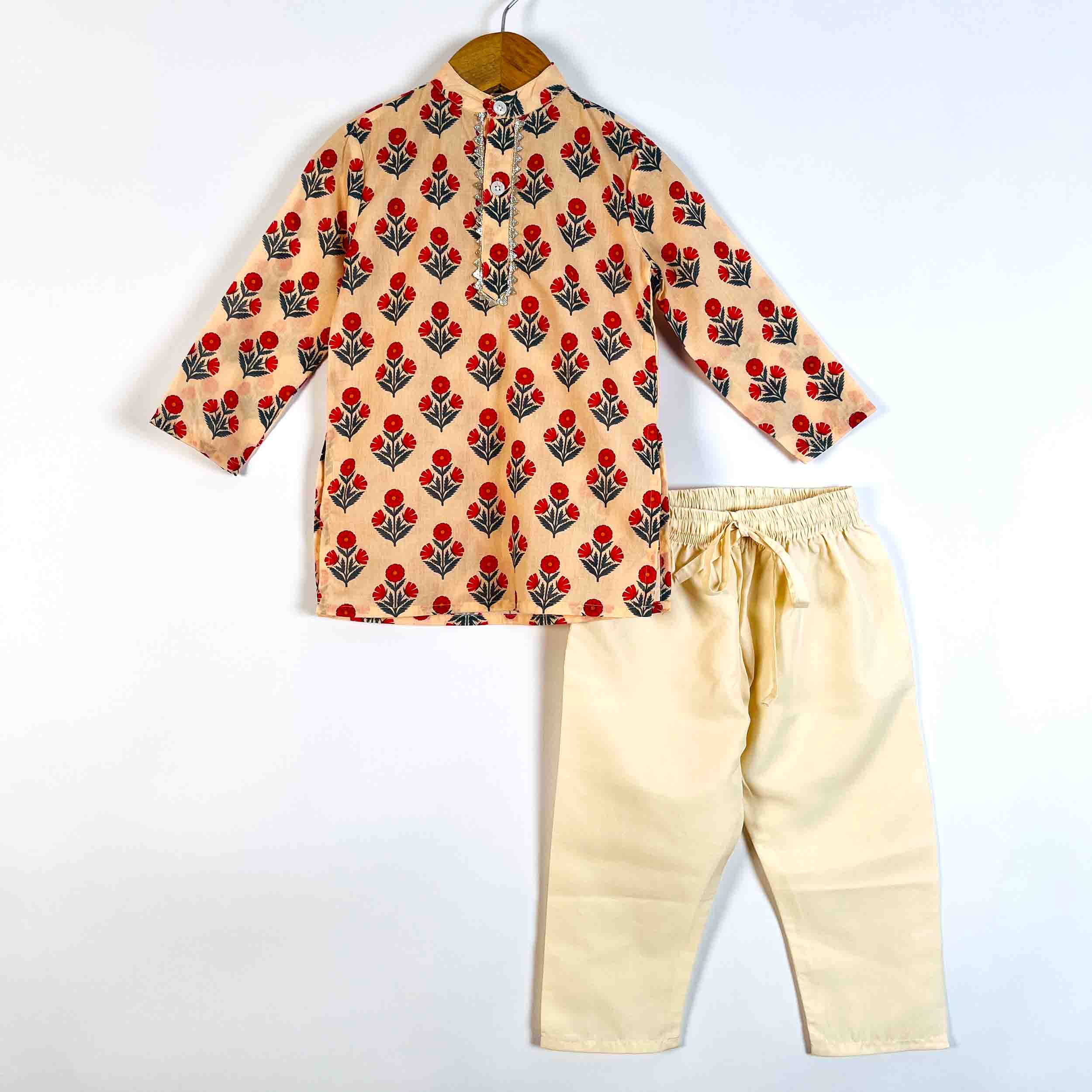 A two-piece children's outfit set consisting of a long-sleeve button-up shirt with a red and black floral block print on a beige background, paired with beige drawstring pants, displayed on a hanger against a white background.