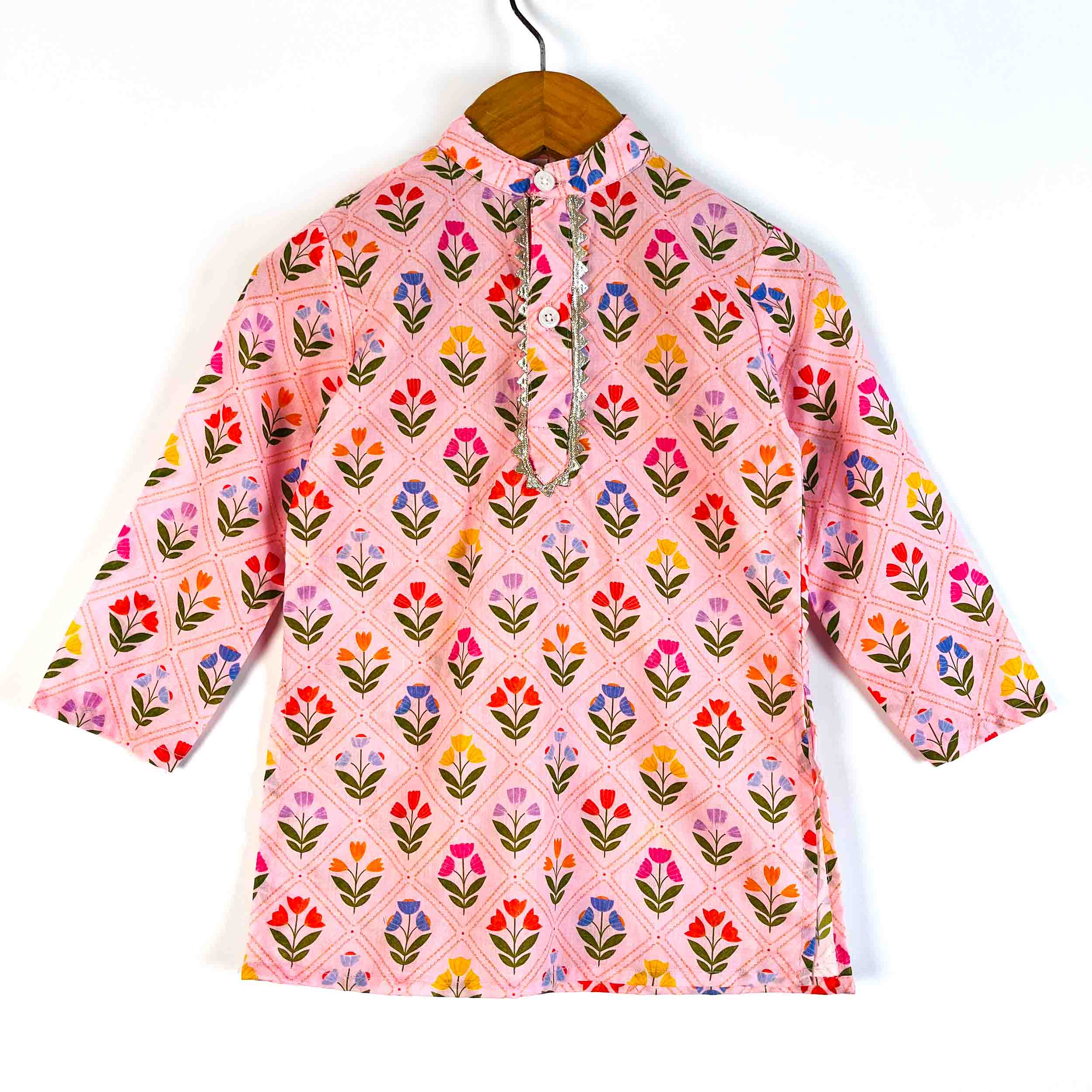 A pink cotton kurta with a colorful floral block print pattern, hanging on a wooden hanger against a plain white background.