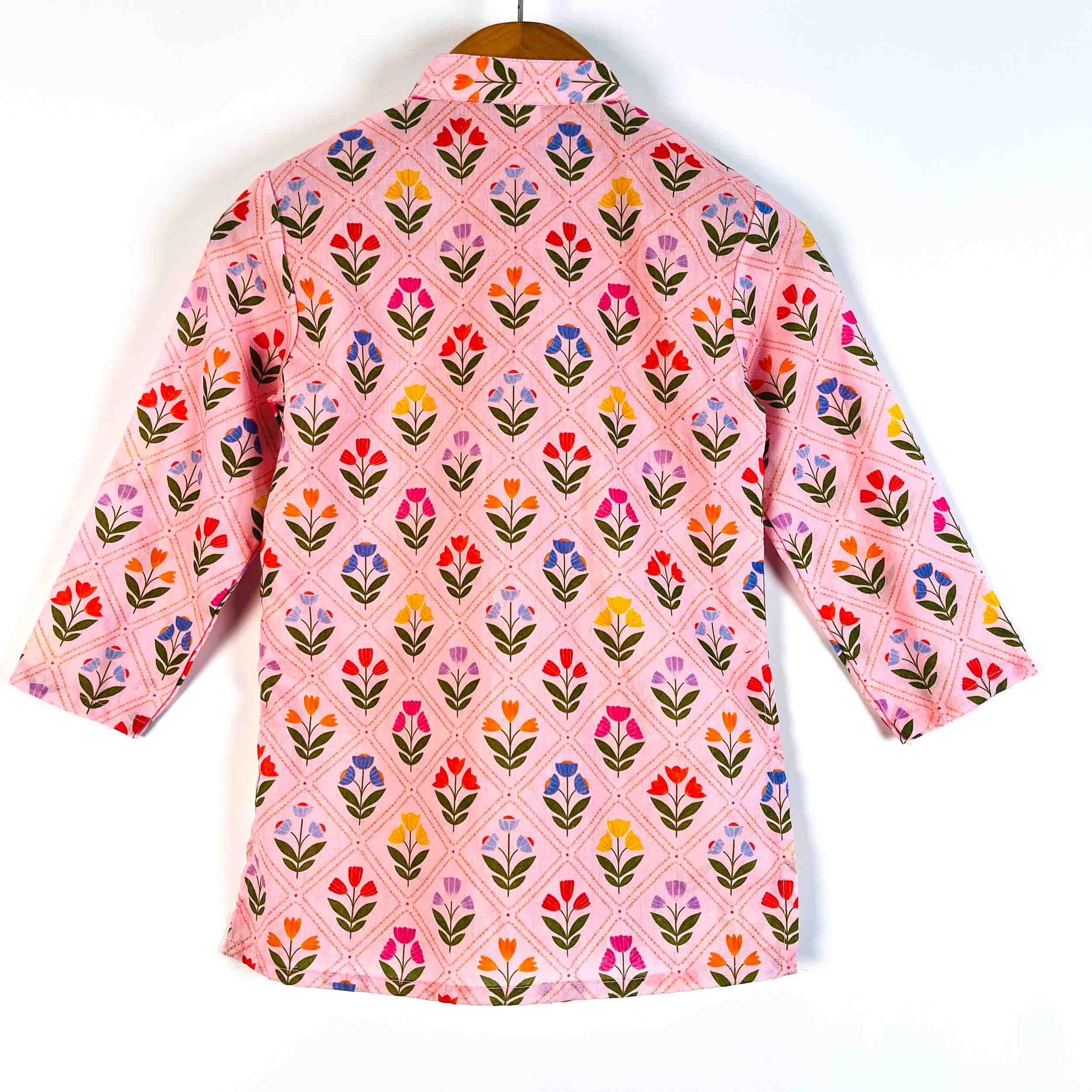 A pink long-sleeve shirt with a colorful floral and diamond pattern, hanging on a wooden hanger against a plain white background.