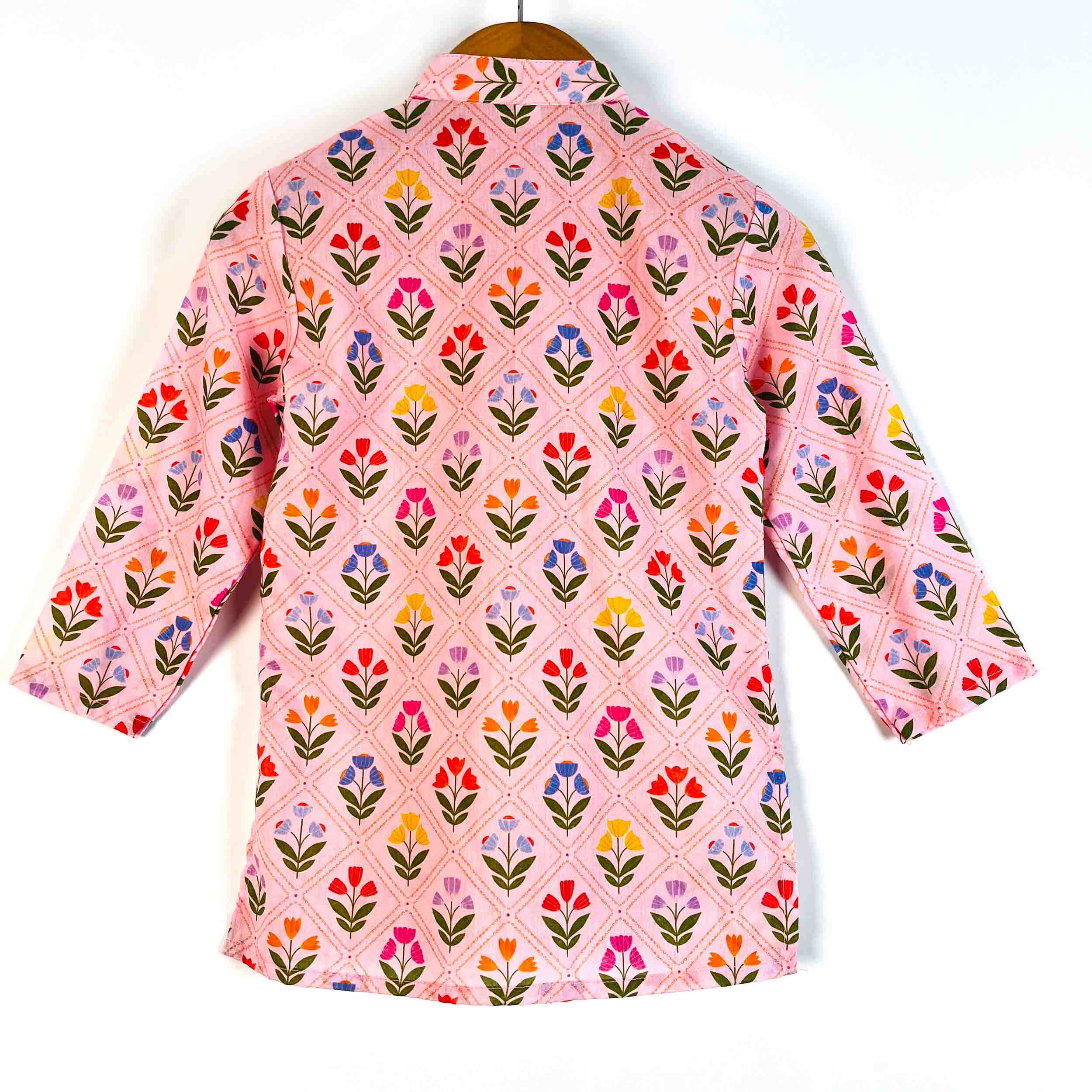 A pink long-sleeve button-up shirt with a colorful floral and geometric pattern, hanging on a wooden hanger against a white background.