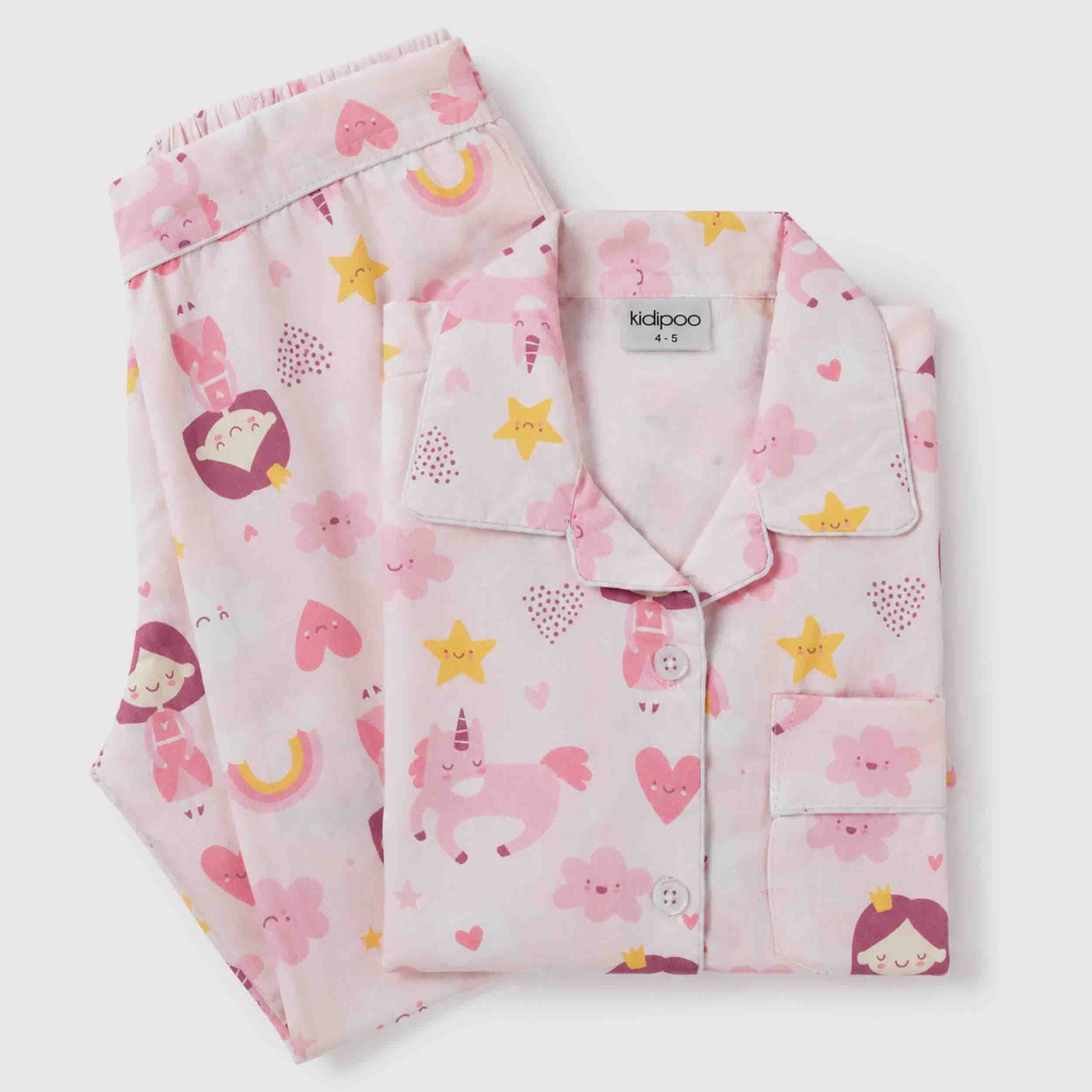 A children's pajama set with a matching button-front top and shorts, printed with a playful pattern of unicorns, stars, hearts, flowers, and cartoon girls in pink, yellow on a very light pink background. The brand name 'kidpoo' is visible on the inner neck label.