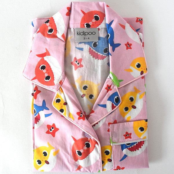 A children's pajama set with long sleeves, featuring a pink background with colorful shark characters and star patterns.