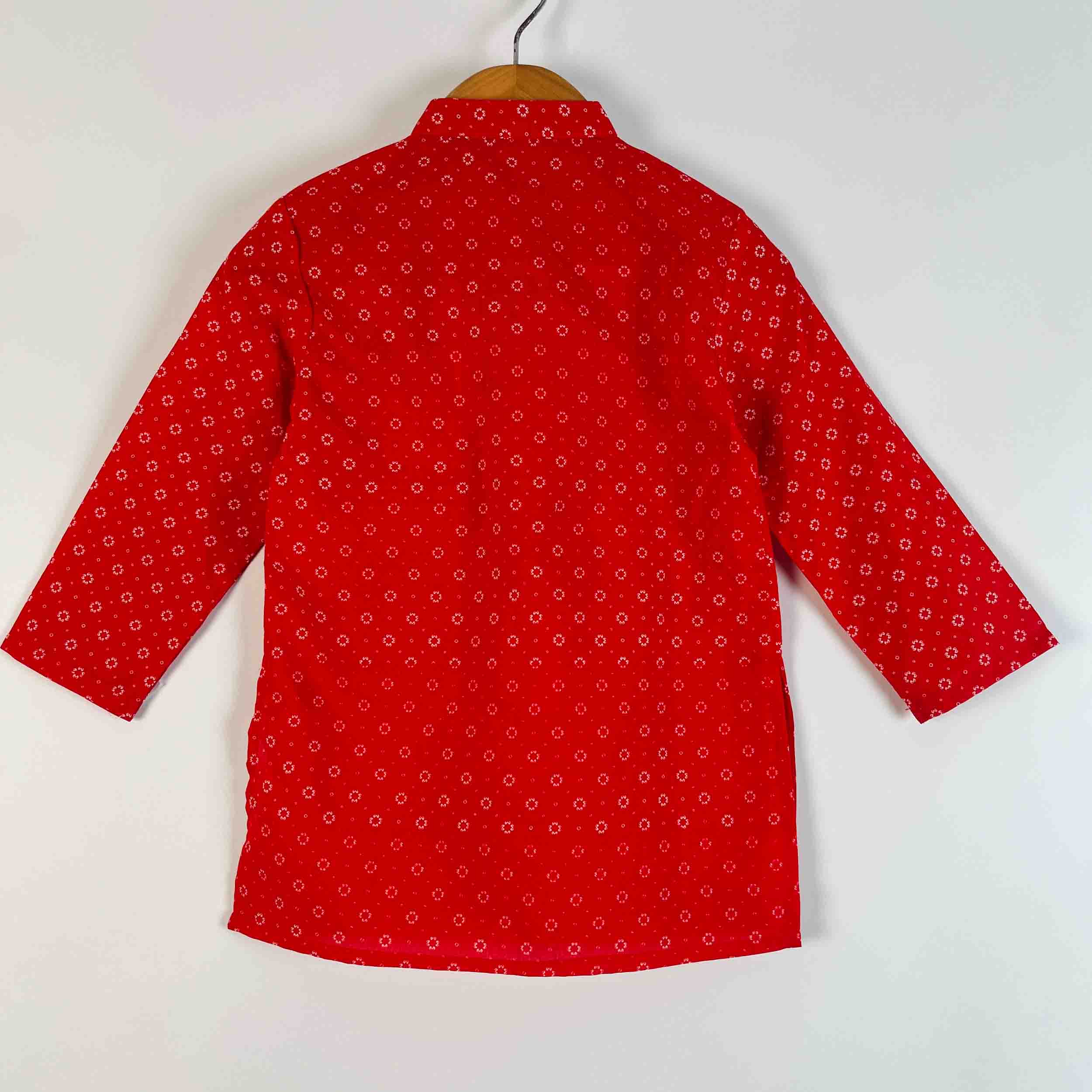 A red long-sleeve shirt with a small white geometric pattern, hanging on a wooden hanger against a plain white background.