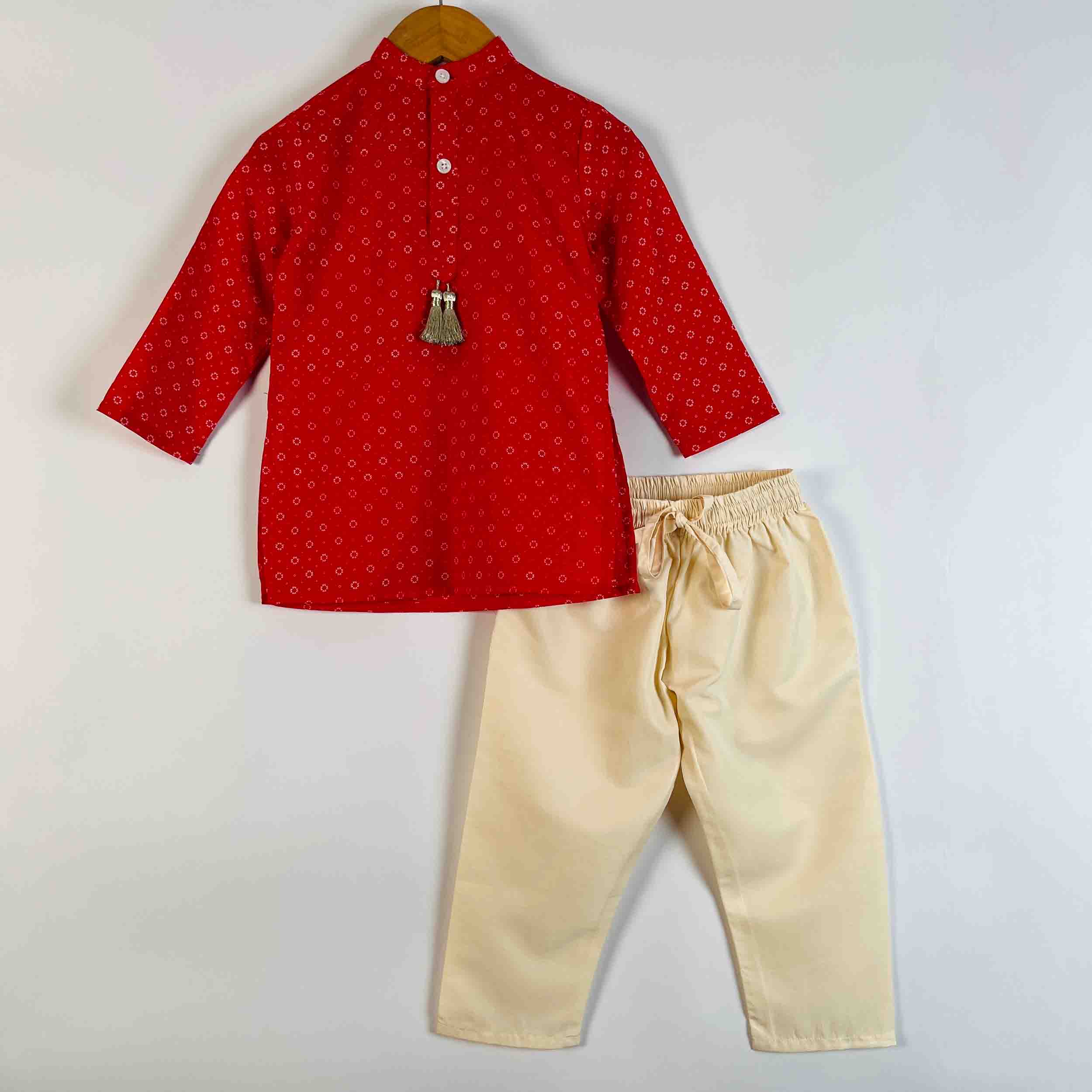 A two-piece children's outfit set consisting of a red long-sleeve kurta with a small white geometric pattern and a silver bell accent, paired with beige drawstring trousers, displayed on a hanger against a plain light background.