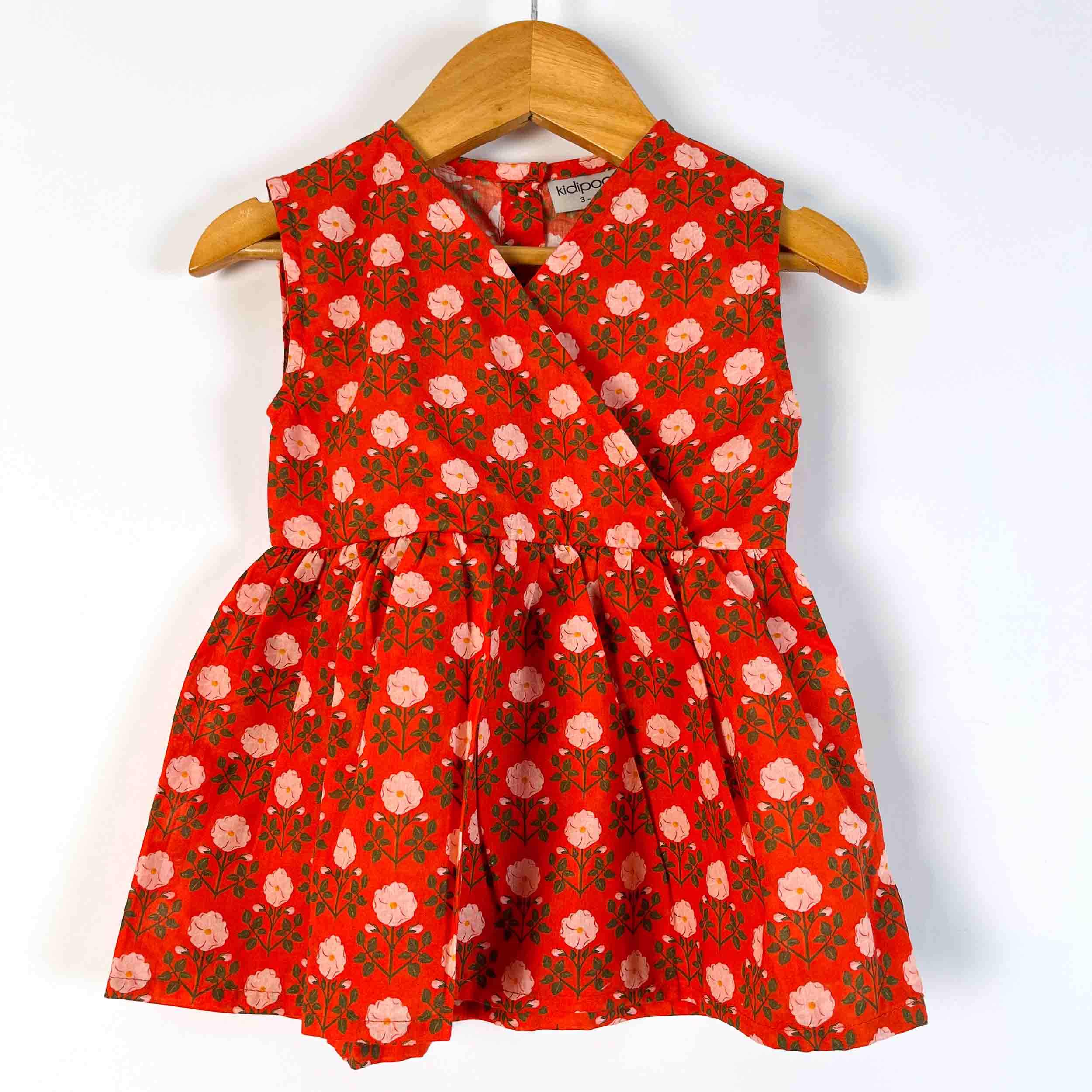 A sleeveless red dress with a pink and green floral print, hanging on a wooden hanger against a plain white background.