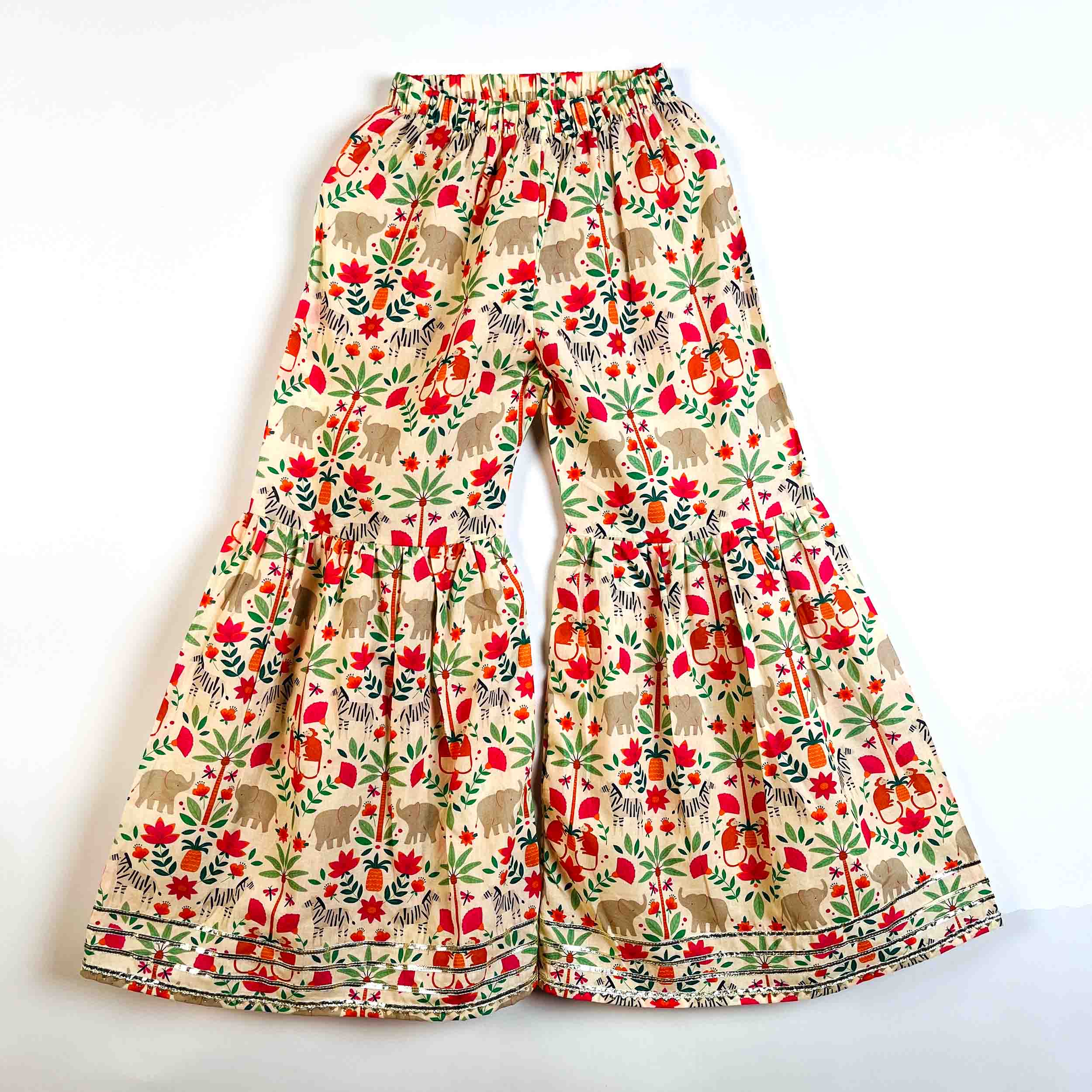 A pair of wide-leg, tiered pants featuring an all-over print of elephants, flowers, and leaves on a cream background. The print includes red, green, orange, and brown details, and the pants are displayed flat against a plain white background.