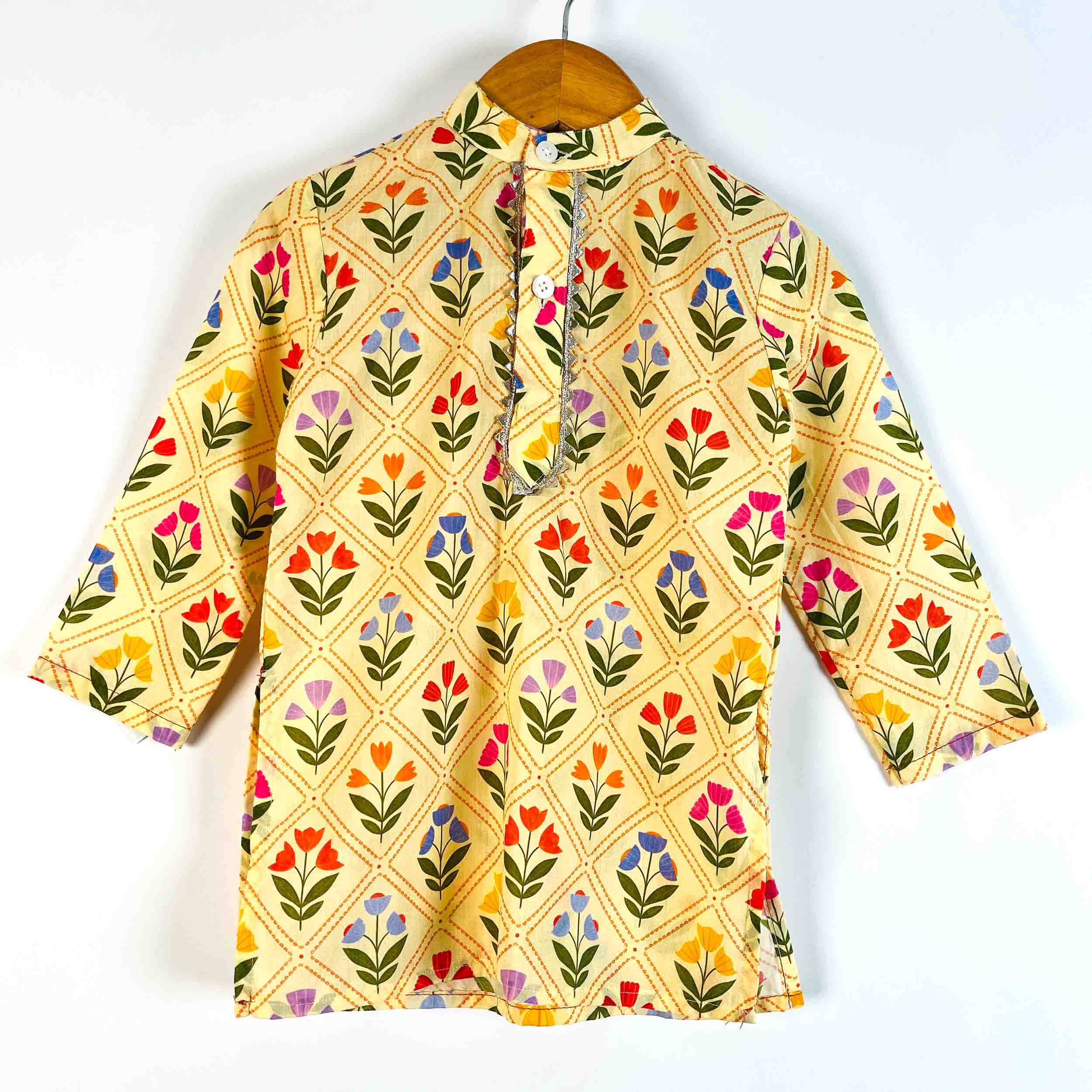 A yellow three-quarter sleeve tunic top with a colorful floral block print, hanging on a wooden hanger against a plain white background.