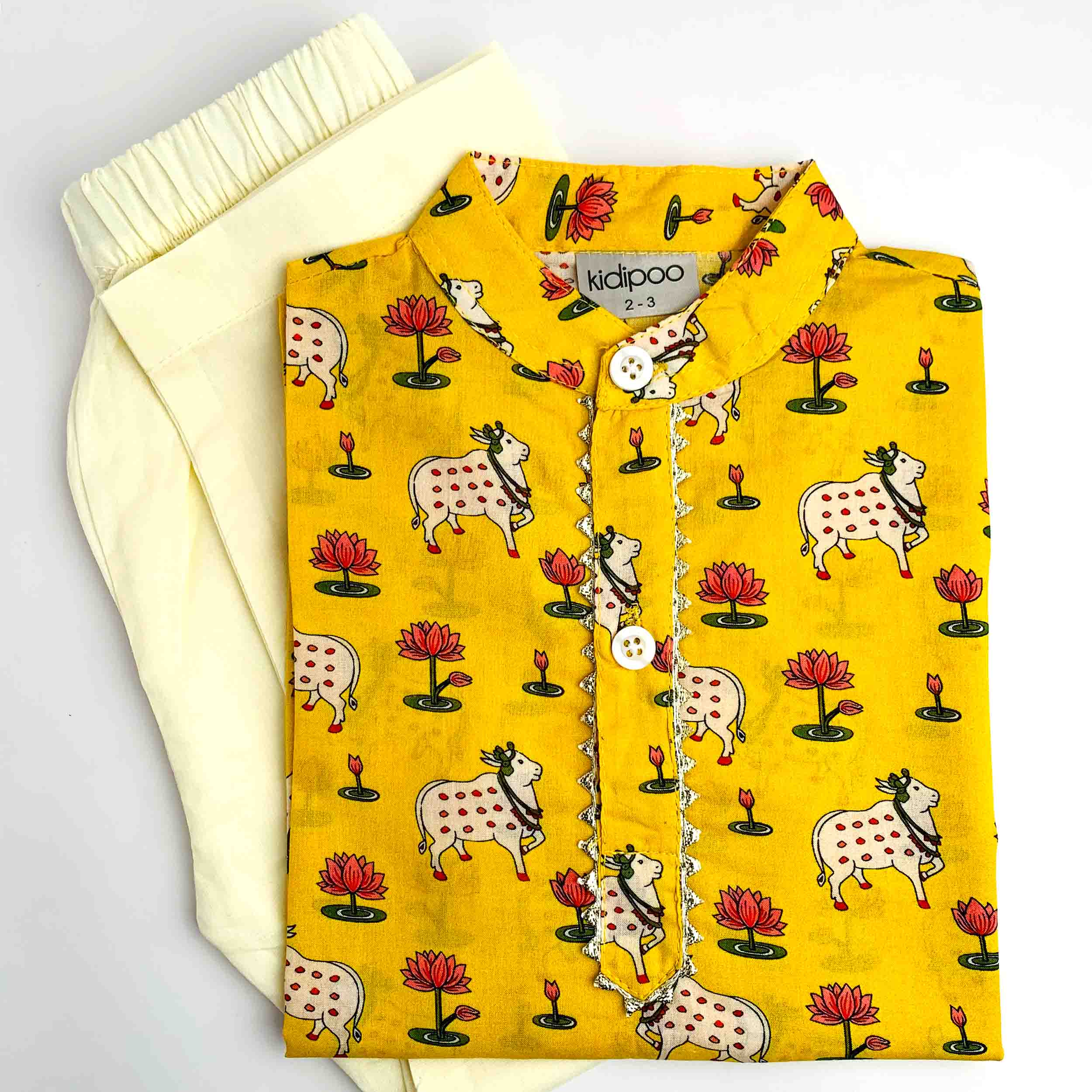 A folded yellow children's kurta pajama set by kidipoo, featuring a cow and lotus print, laid flat next to a matching cream-colored pajama pants piece on a white background.
