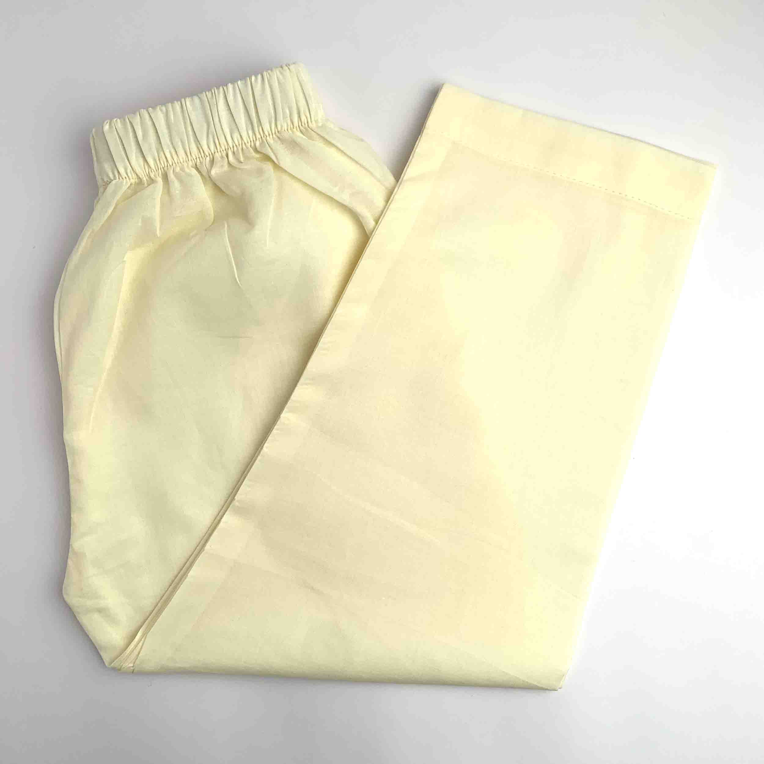 A pair of light cream or pale yellow lounge pants with an elastic waistband, folded on a light gray background.