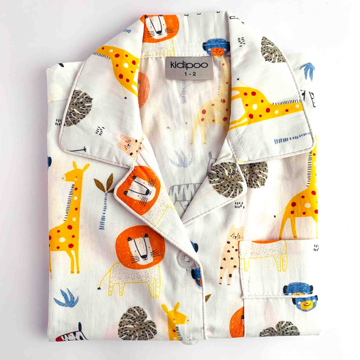 A folded children's pajama shirt with a safari animal print, featuring giraffes, lions, and zebras on a white background. The brand label 'kidpoo 1-2' is visible at the collar.