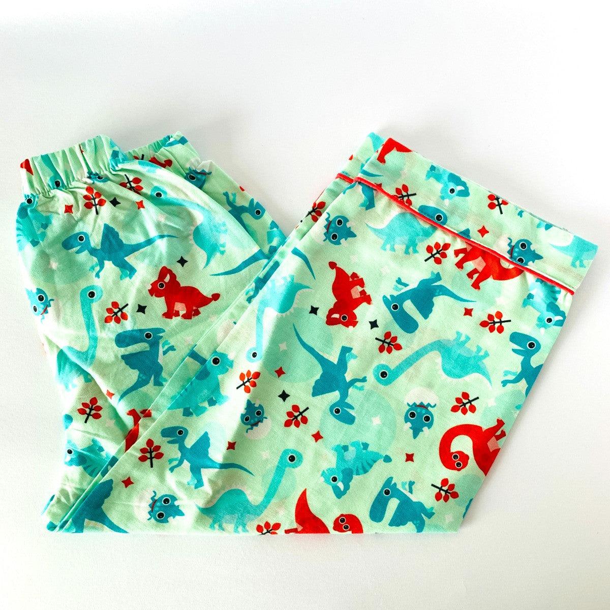 A baby night suit with dinosaur print, consisting of a long sleeve shirt and pajamas with elastic at the waist, laid flat on a white background.