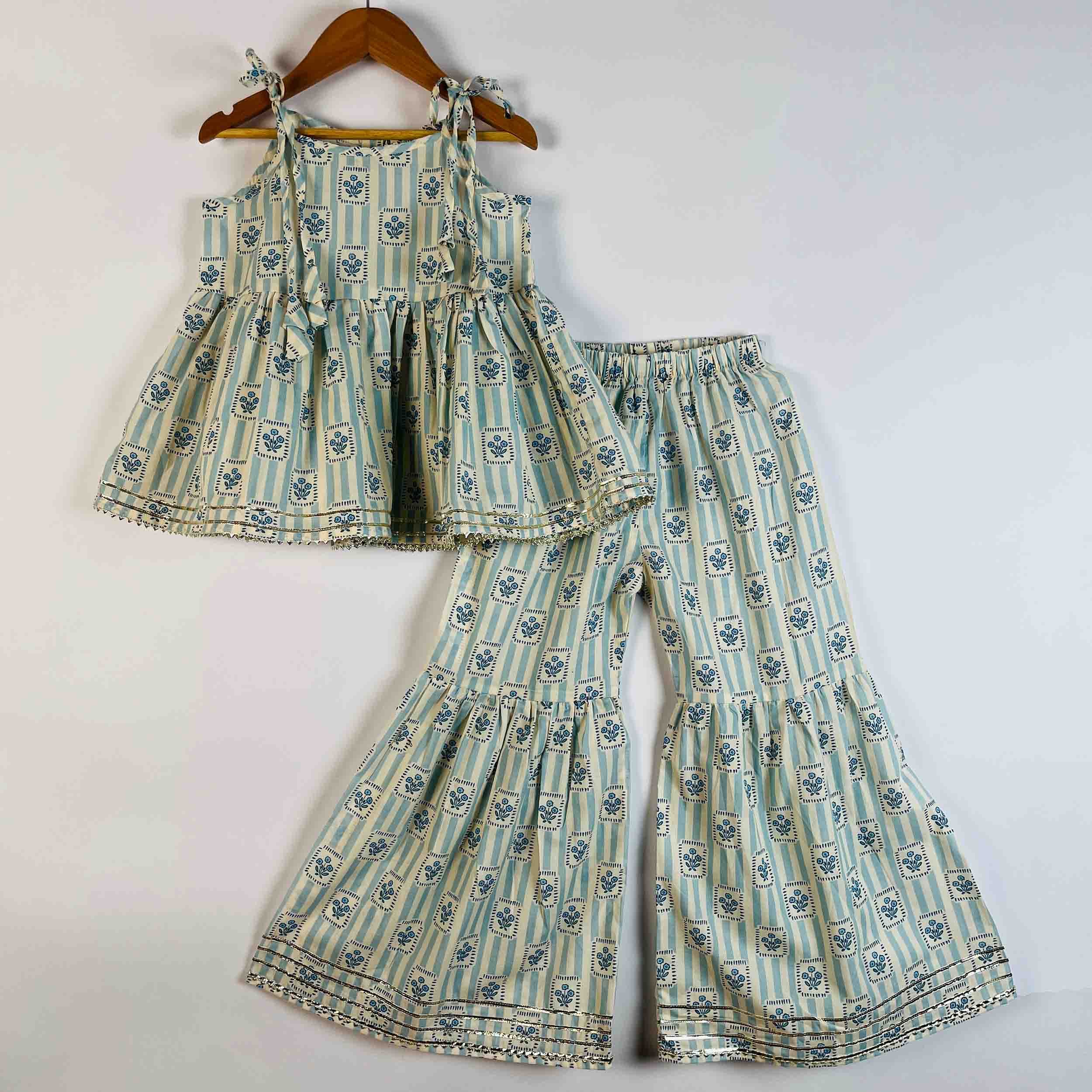 A two-piece toddler girl's outfit set consisting of a sleeveless tiered peplum top and matching wide-leg flared pants, both featuring a light blue and white striped pattern with small blue floral motifs and decorative borders. The set is displayed on a wooden hanger against a plain white background.