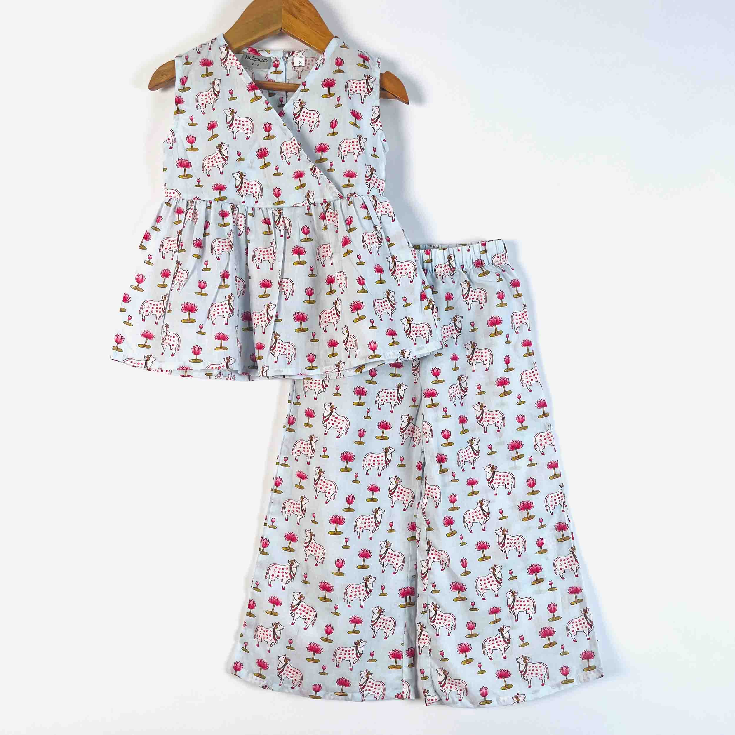 A two-piece children's outfit set consisting of a sleeveless peplum-style top and matching wide-leg pants, both printed with a light gray background and a repeating pattern of pink flowers, brown trees, and white deer. The set is displayed on a wooden hanger against a plain white background.