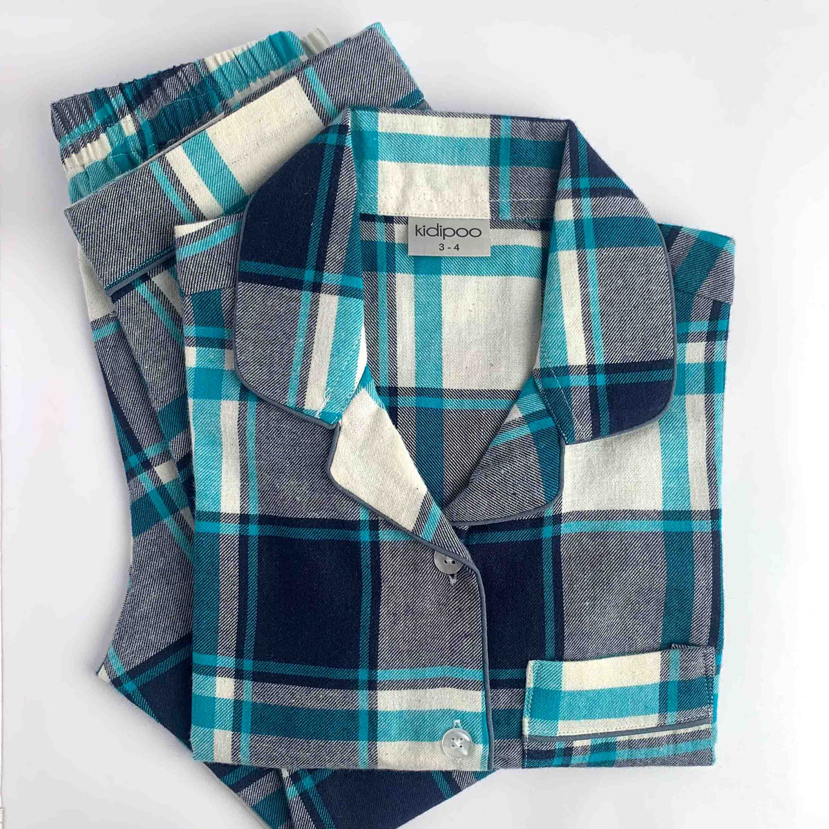 A folded plaid pajama set with a collared shirt and matching pants on a plain white background. The fabric has a tartan pattern in navy blue, teal, gray, and off-white.