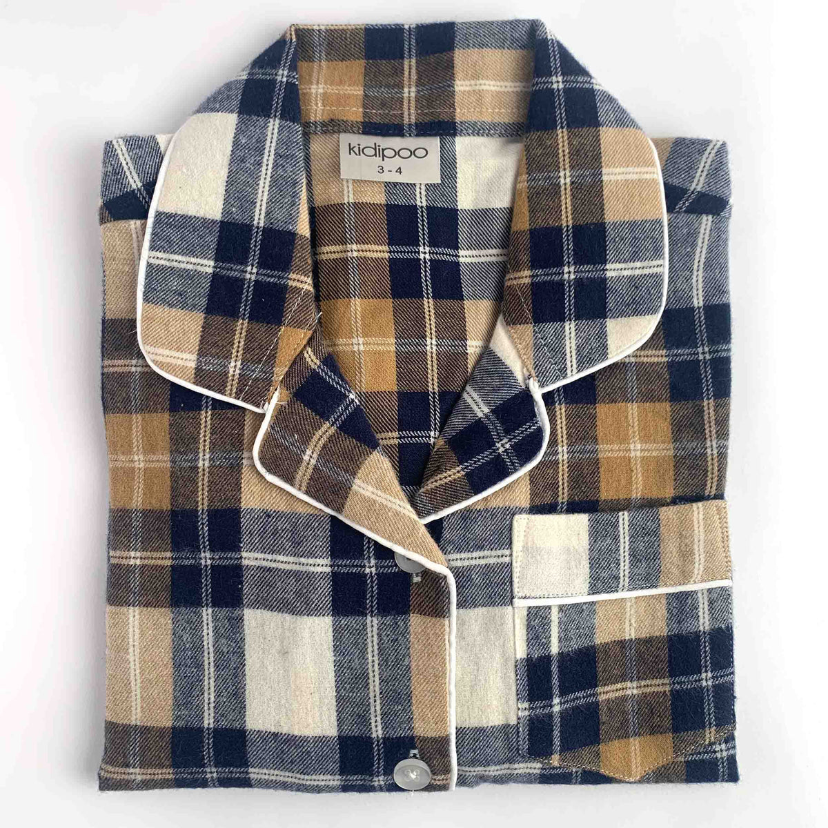 A folded plaid pajama shirt on a white background, featuring a navy, tan, and cream check pattern with white piping and a visible 'kidipoo' brand label.