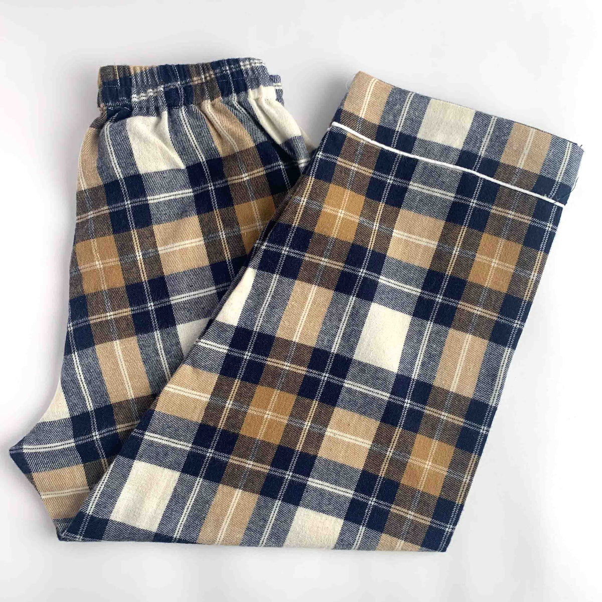 A pair of folded plaid pajama pants in a navy blue, tan, and cream tartan pattern, laid flat on a white background.