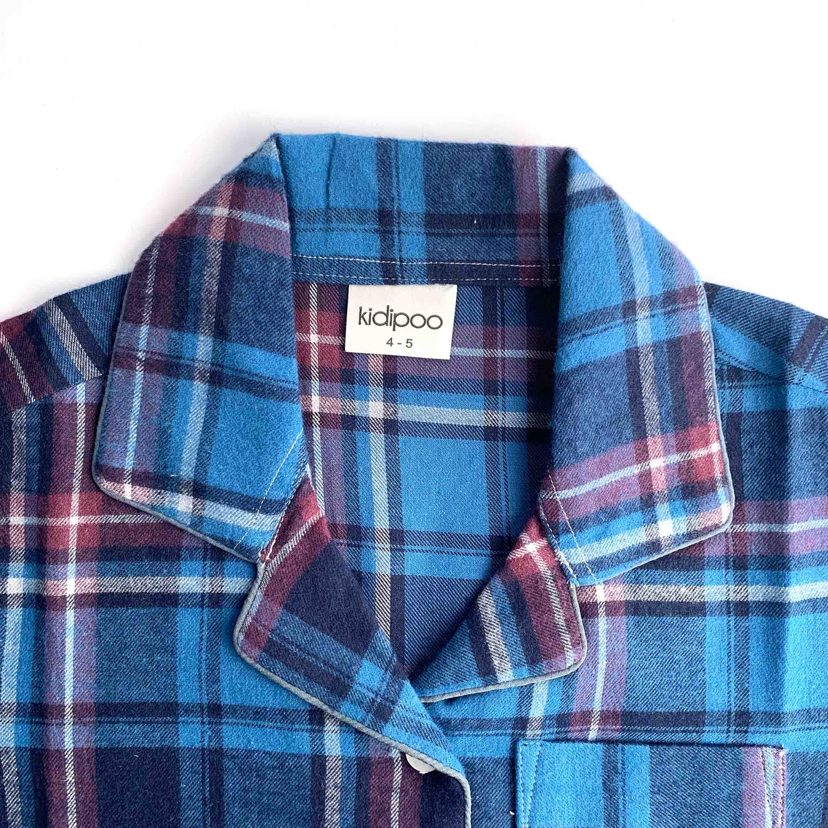 A close-up of a children's plaid shirt collar with a white brand label reading 'kidipoo' on a plain white background.