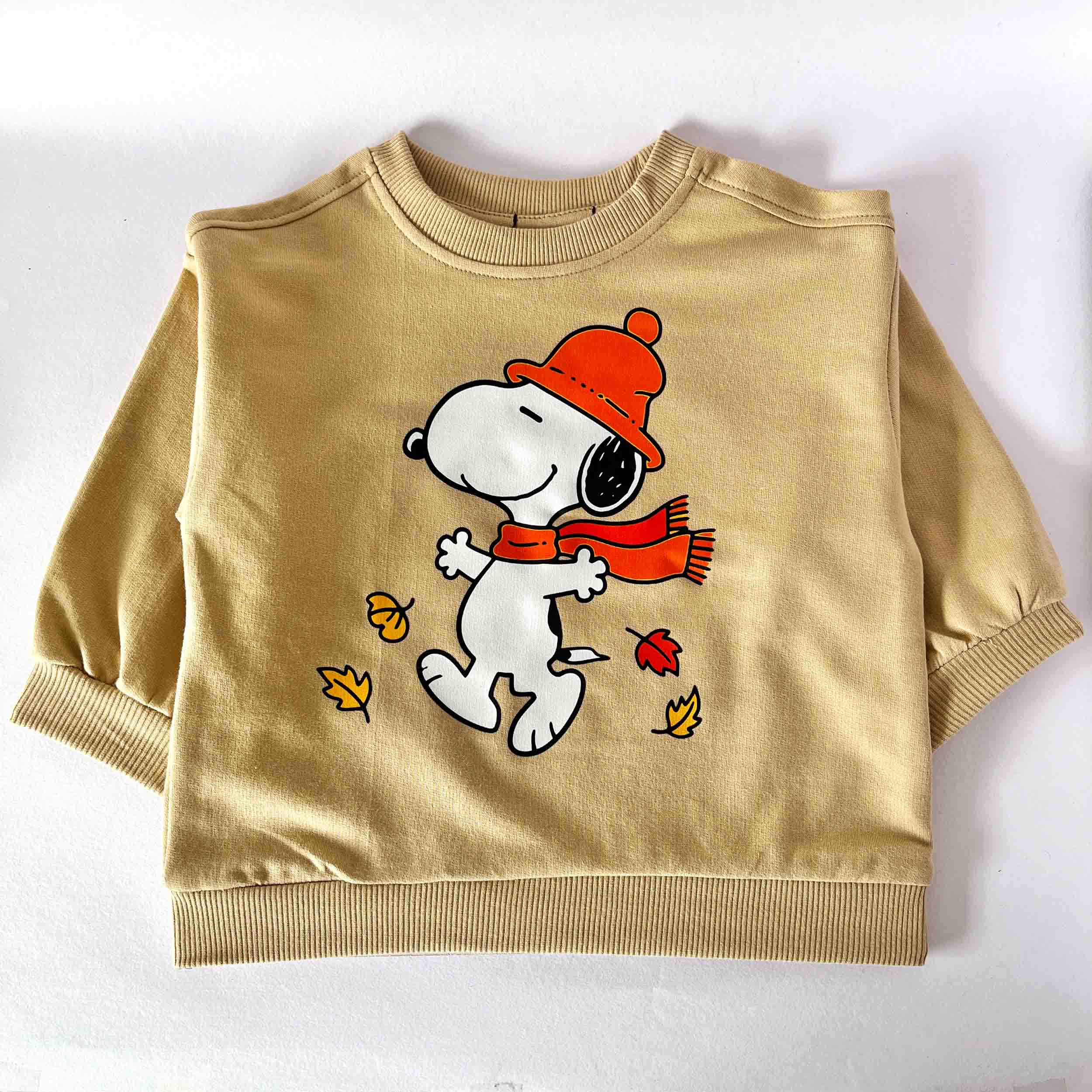 Beige sweatshirt with a cartoon dog wearing an orange hat and scarf on a white background