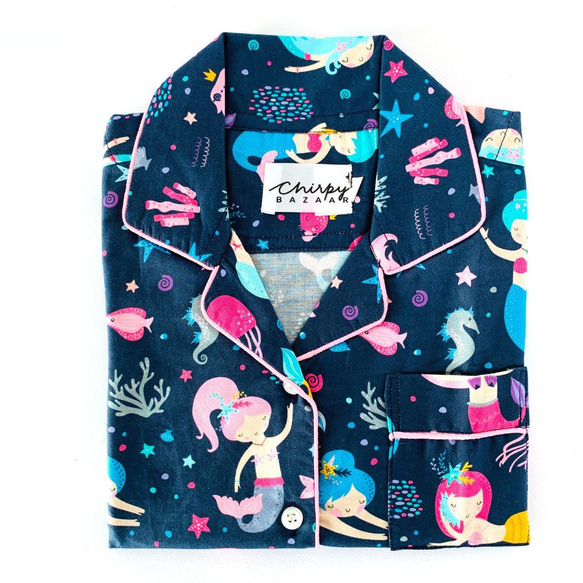 A set of children's sleepwear featuring a long sleeve shirt and pajamas with elastic at the waist, decorated with colorful dancing mermaids and stars