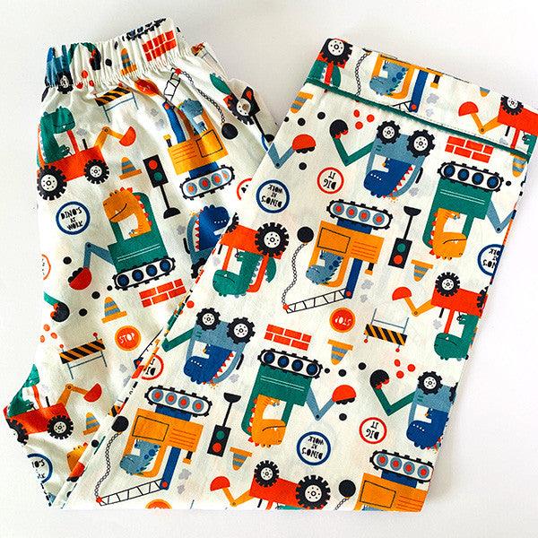 A set of children's pajamas with a dinosaur theme, including a long sleeve, front button shirt and coordinated pajamas with elastic at the waist, laid out on a white surface.