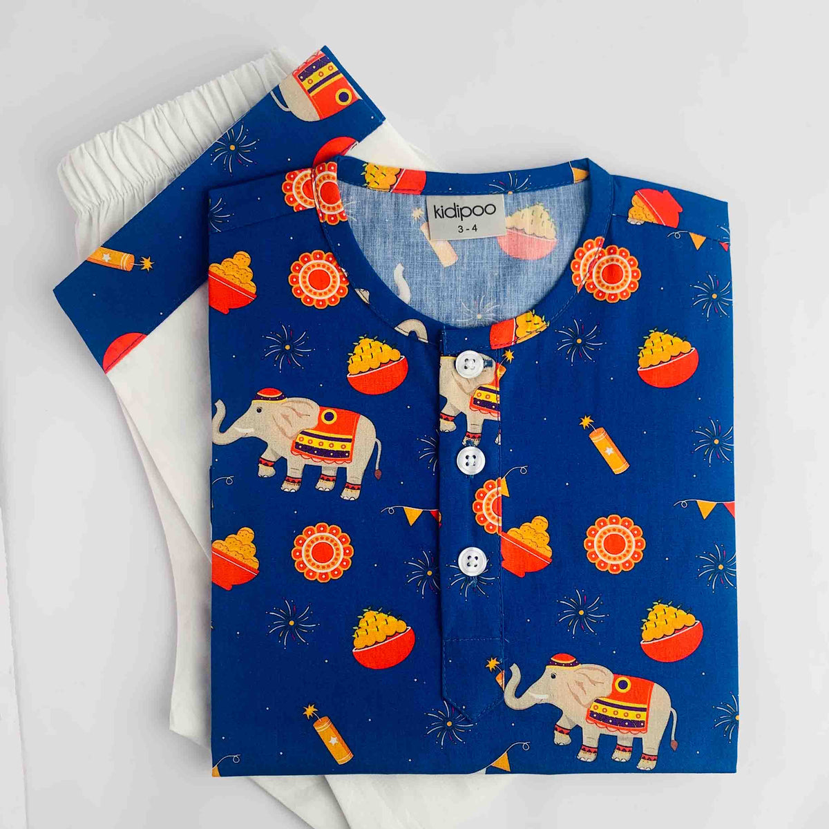 A folded children's long-sleeve top and matching pants set from the brand kidpoo, featuring a festive Indian theme. The fabric is royal blue with a print of elephants, acorns, fireworks, and party hats, with a white inner lining and white buttons.