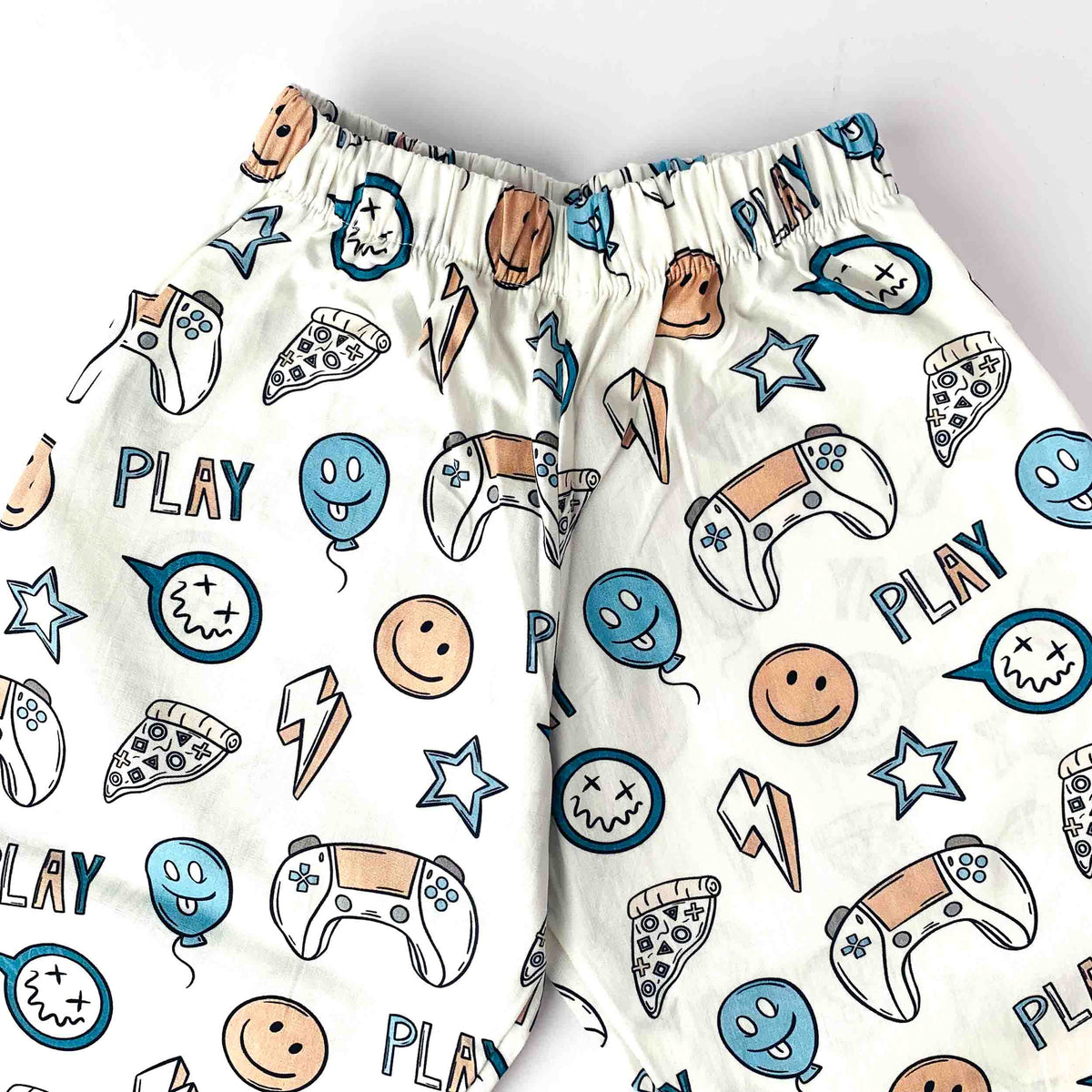 White elastic waist shorts with a colorful gaming-themed print featuring game controllers, pizza slices, smiley faces, stars, and the word 'PLAY'.