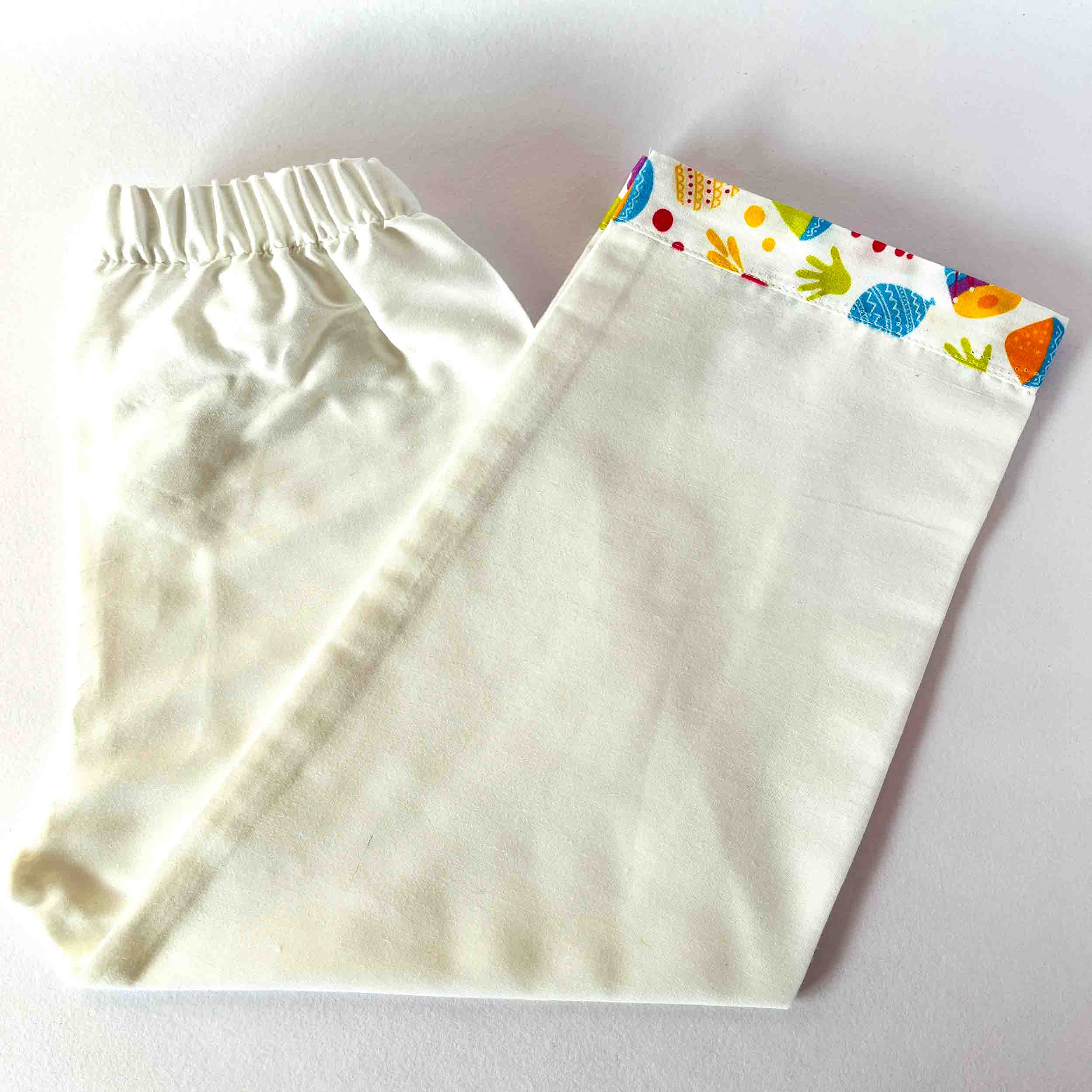 White baby pants with colorful handprint pattern on a white background