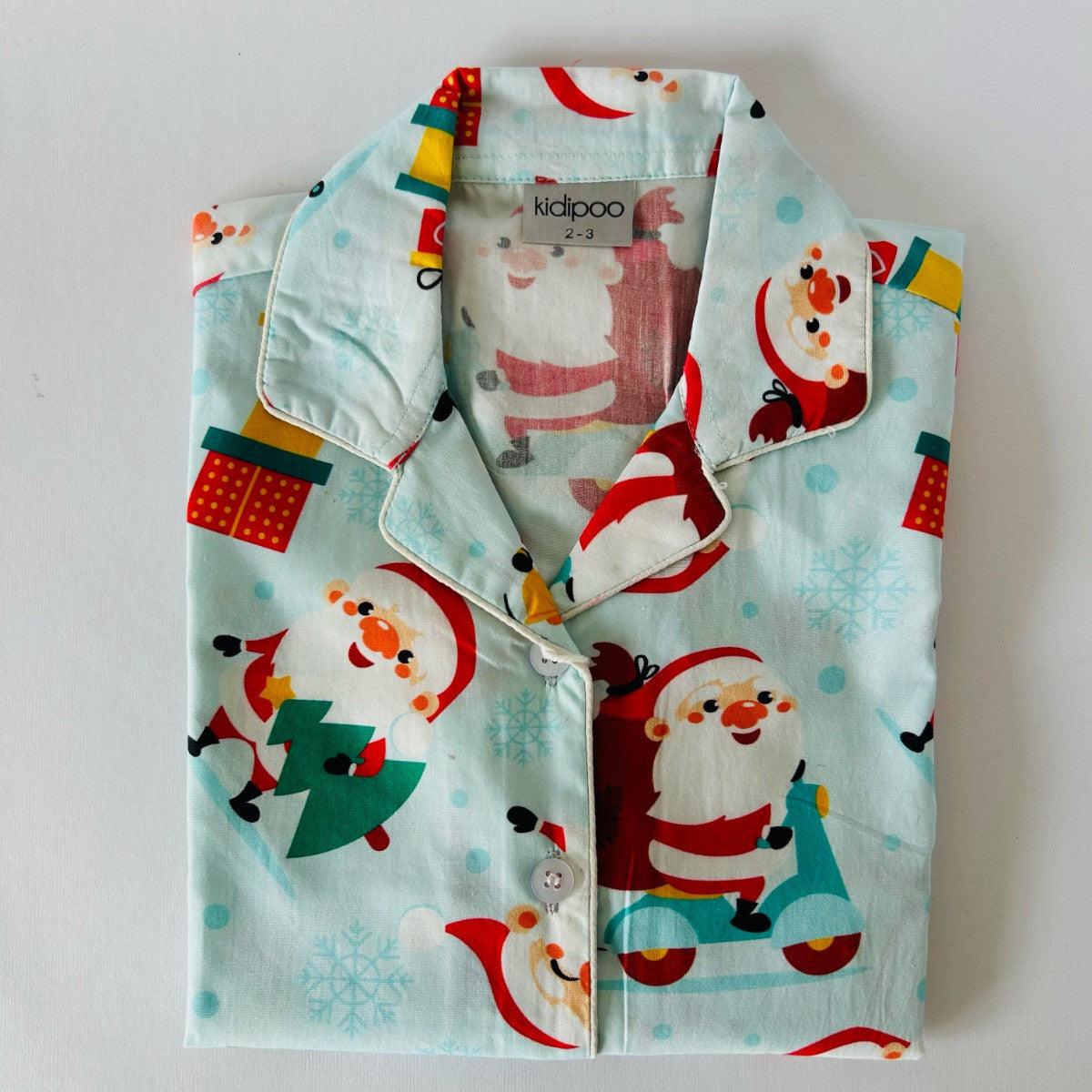 A Christmas-themed sleepwear set, consisting of a long sleeve shirt and pajamas, with Santa Claus and holiday motifs on a light blue background.