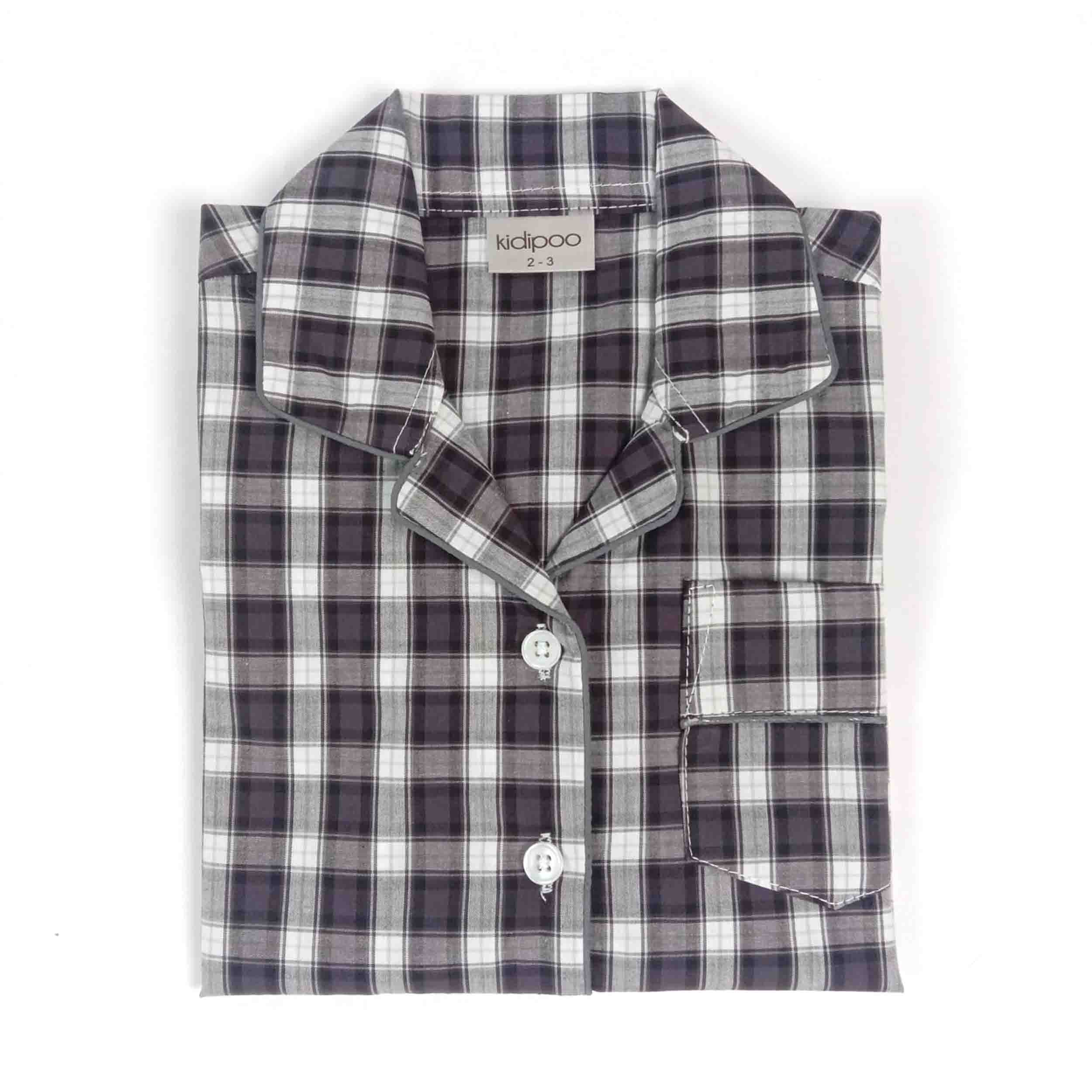 A folded long-sleeve pajama shirt with a dark gray, white, and black plaid pattern, featuring a collar, button front, and a chest pocket. The brand label 'udipoo' is visible inside the collar.