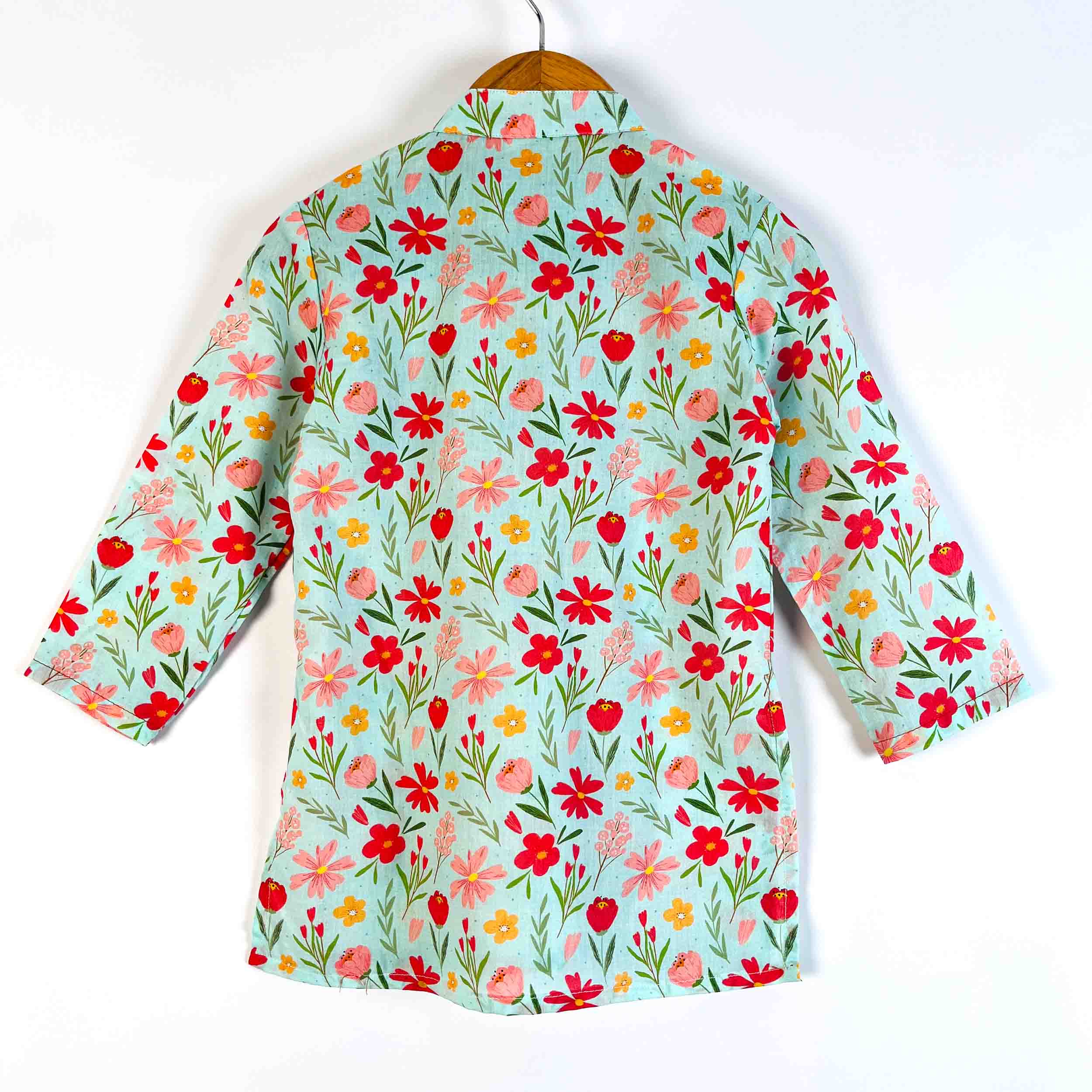 A long-sleeve button-up shirt with a vibrant floral print, hanging on a wooden hanger against a plain white background. The shirt features a light mint green base with red, pink, and yellow flowers and green stems.