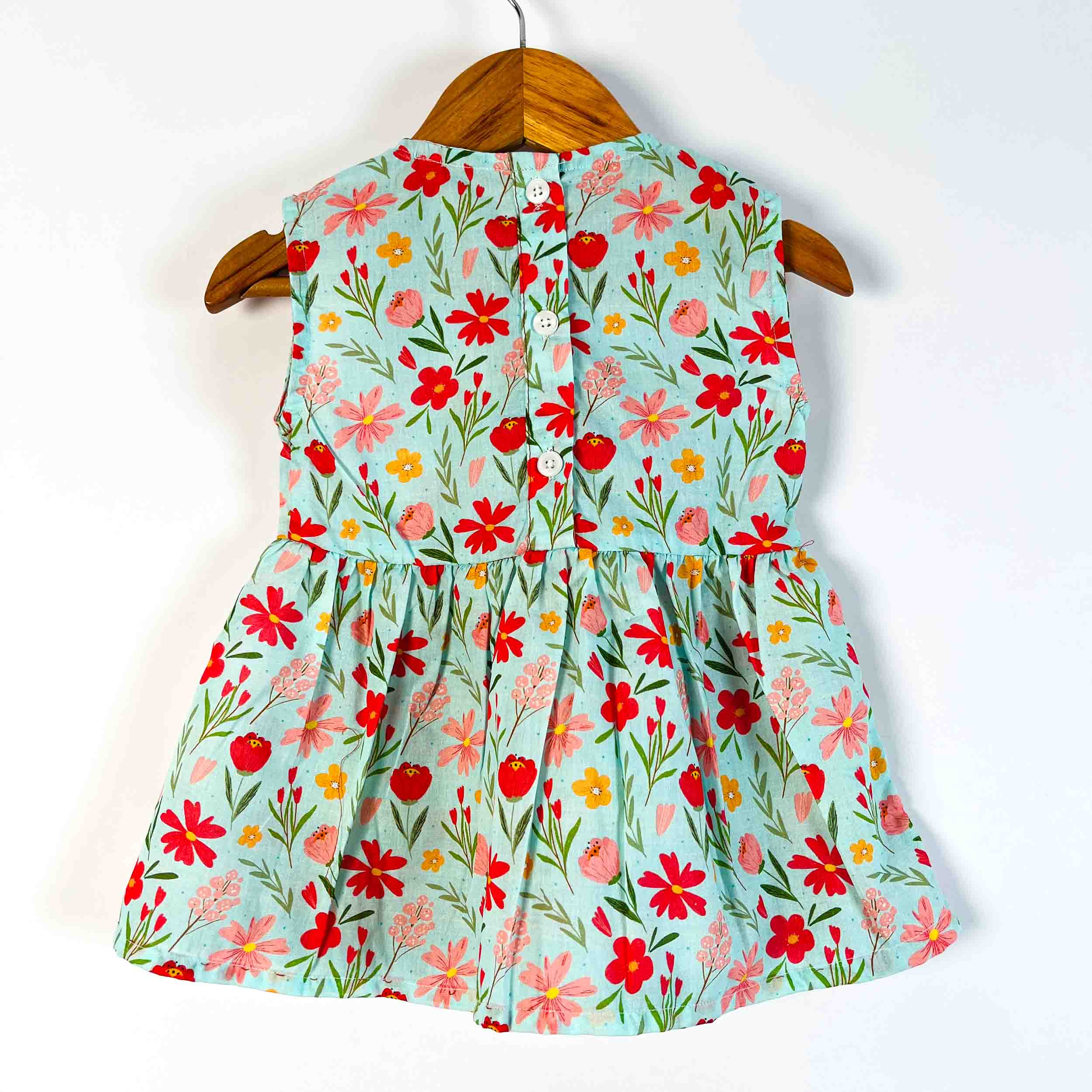 A sleeveless light blue children's dress with a vibrant red, pink, and yellow floral print, hanging on a wooden hanger against a plain white background.