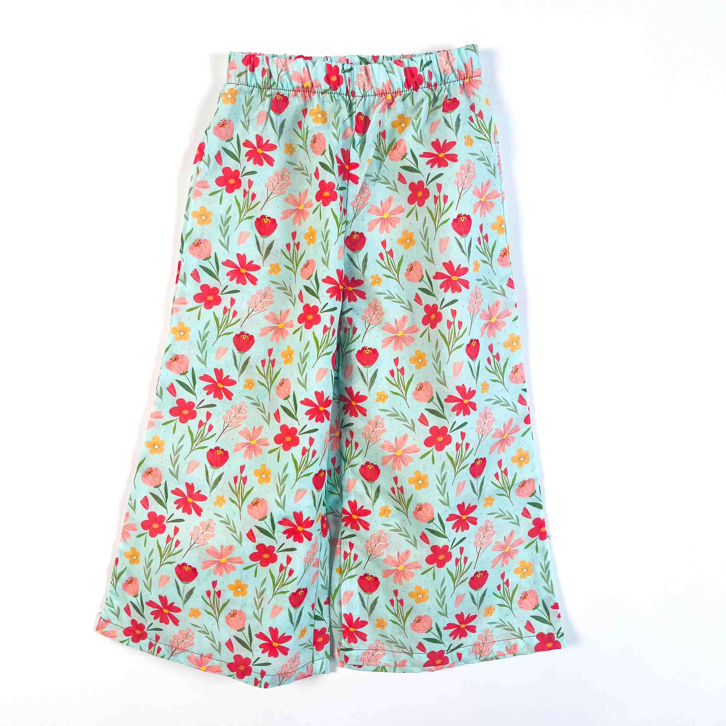 A pair of wide-leg cropped pants featuring a colorful floral print on a light blue background, laid flat against a white background.