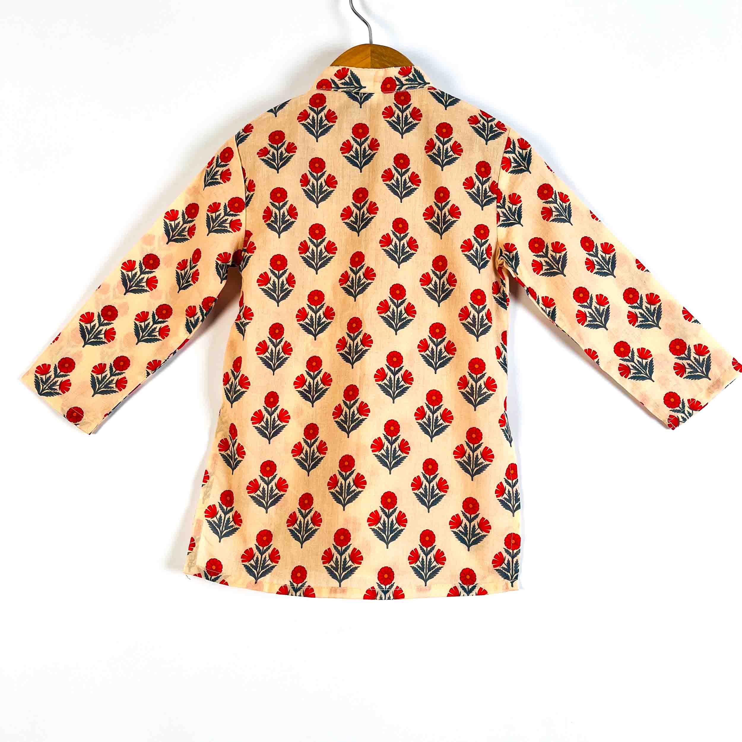 A long-sleeve shirt with a beige base and a repeating red and green floral block print, hanging on a wooden hanger against a white background.