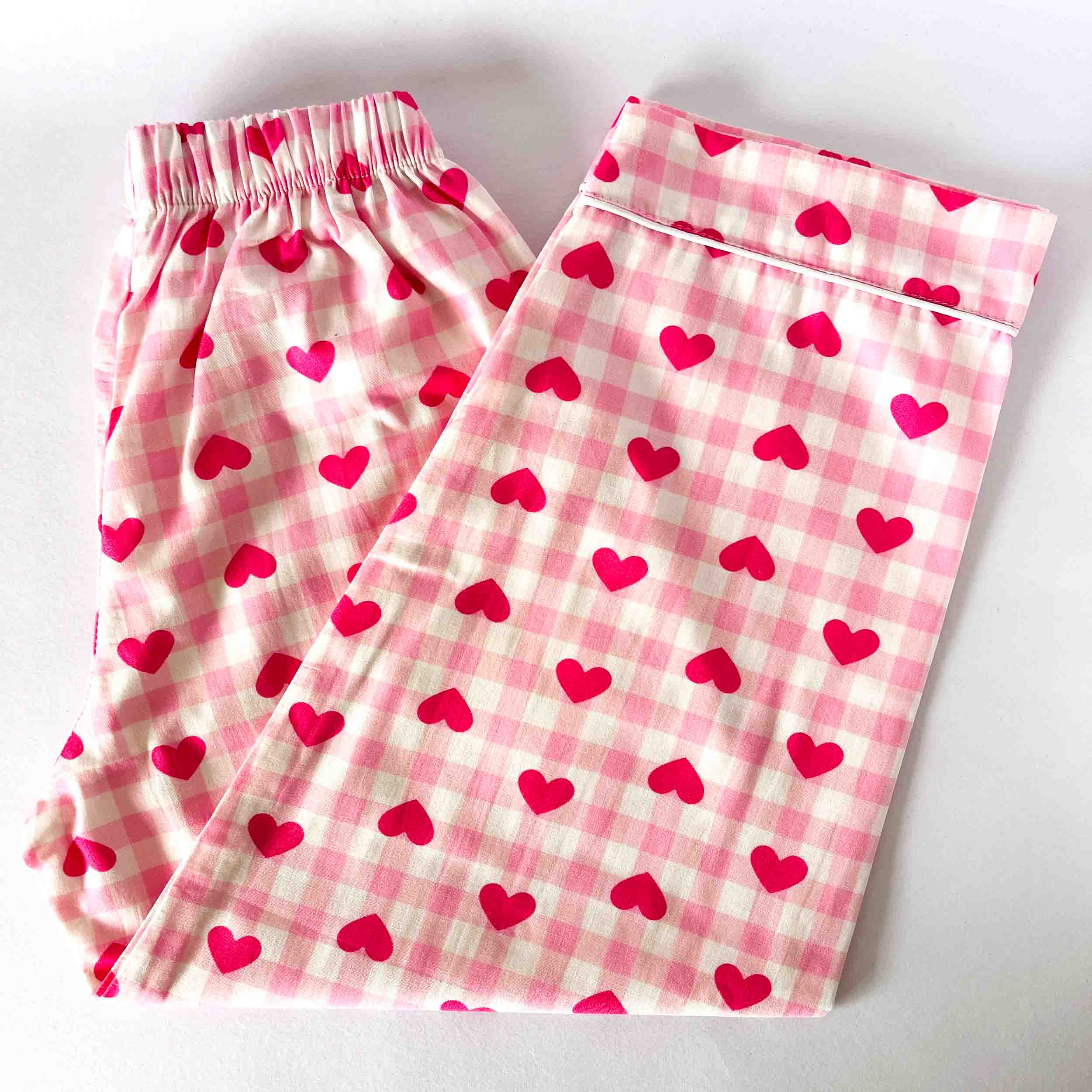 Pink pajama pants with heart and checkered patterns on a white background