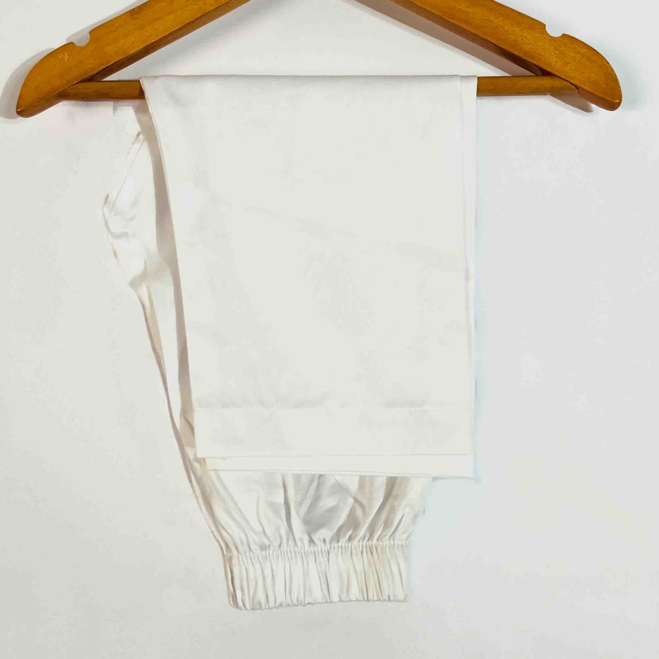 A pair of white elastic-waist pants or shorts hanging from a wooden hanger against a plain white background.