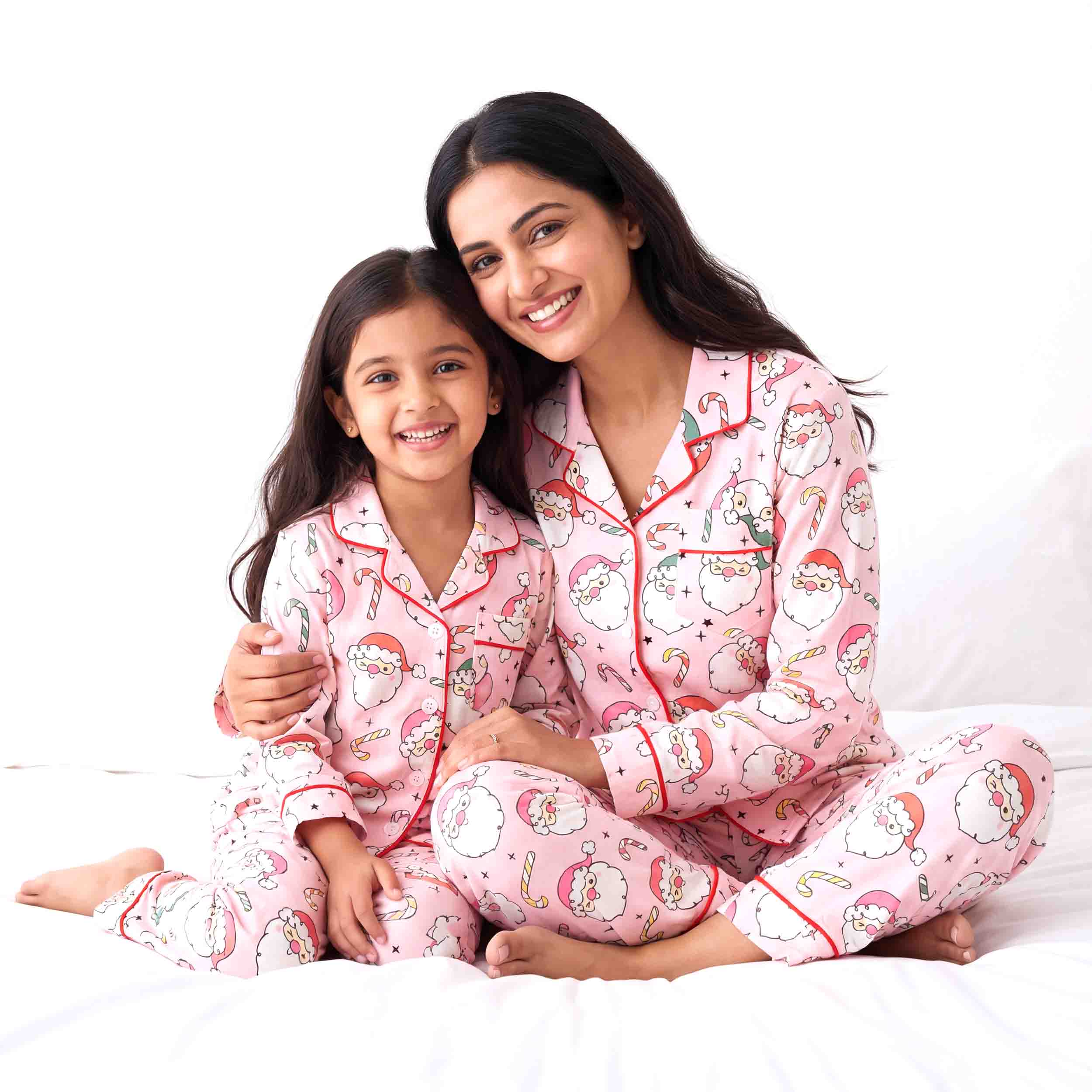 Mother and daughter wearing matching pink Santa print cotton night suits sitting together