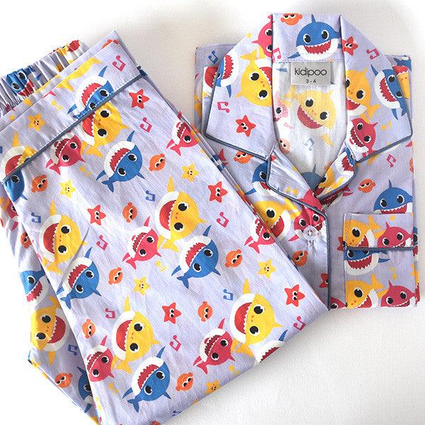 A child's sleepwear set with a long sleeve shirt and pajamas featuring a colorful shark pattern on a light background.