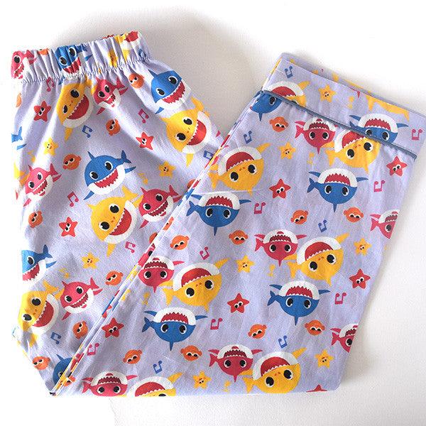 A child's sleepwear set with a long sleeve shirt and pajamas featuring a colorful shark pattern on a light background.