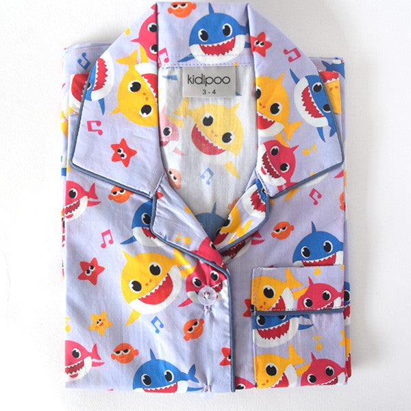 A child's sleepwear set with a long sleeve shirt and pajamas featuring a colorful shark pattern on a light background.