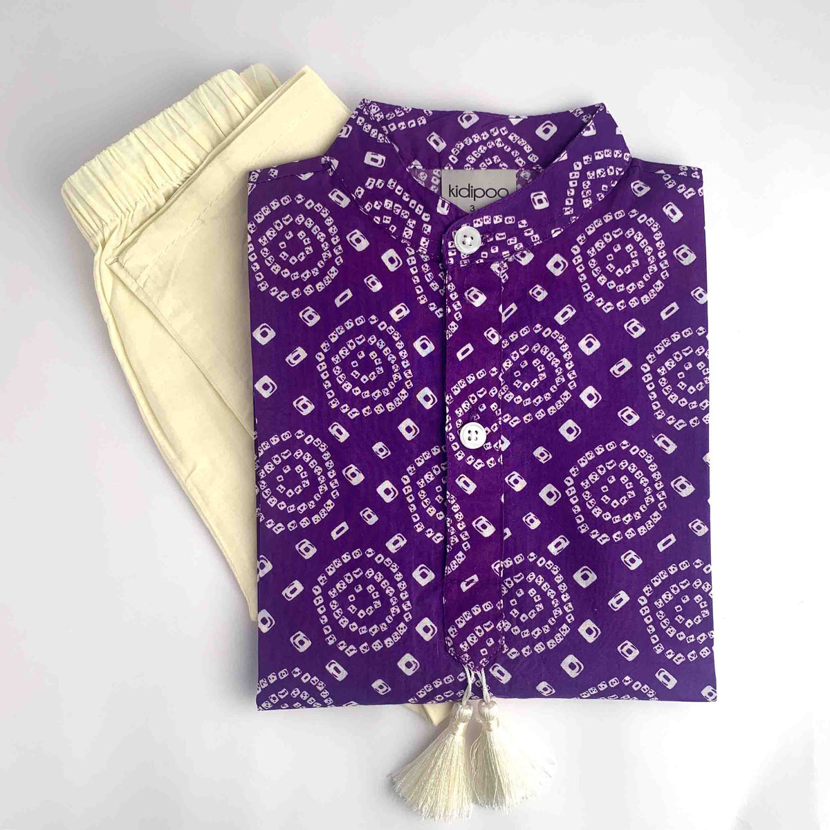 Purple Bandhani Kurta Pajama for Kids with white Bandhani print, button-up kurta, cream pajama and cream tassel on a white background.