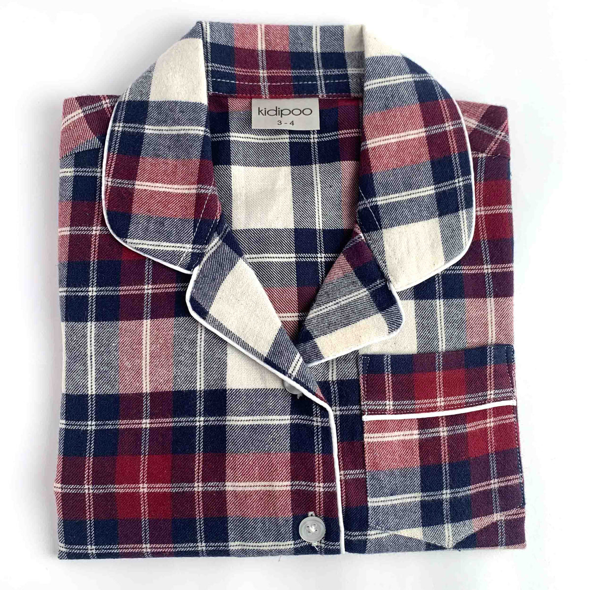 A folded plaid pajama shirt with a collar and button closure, shown on a plain white background. The fabric has a tartan pattern in red, navy blue, and cream, with white piping along the edges.