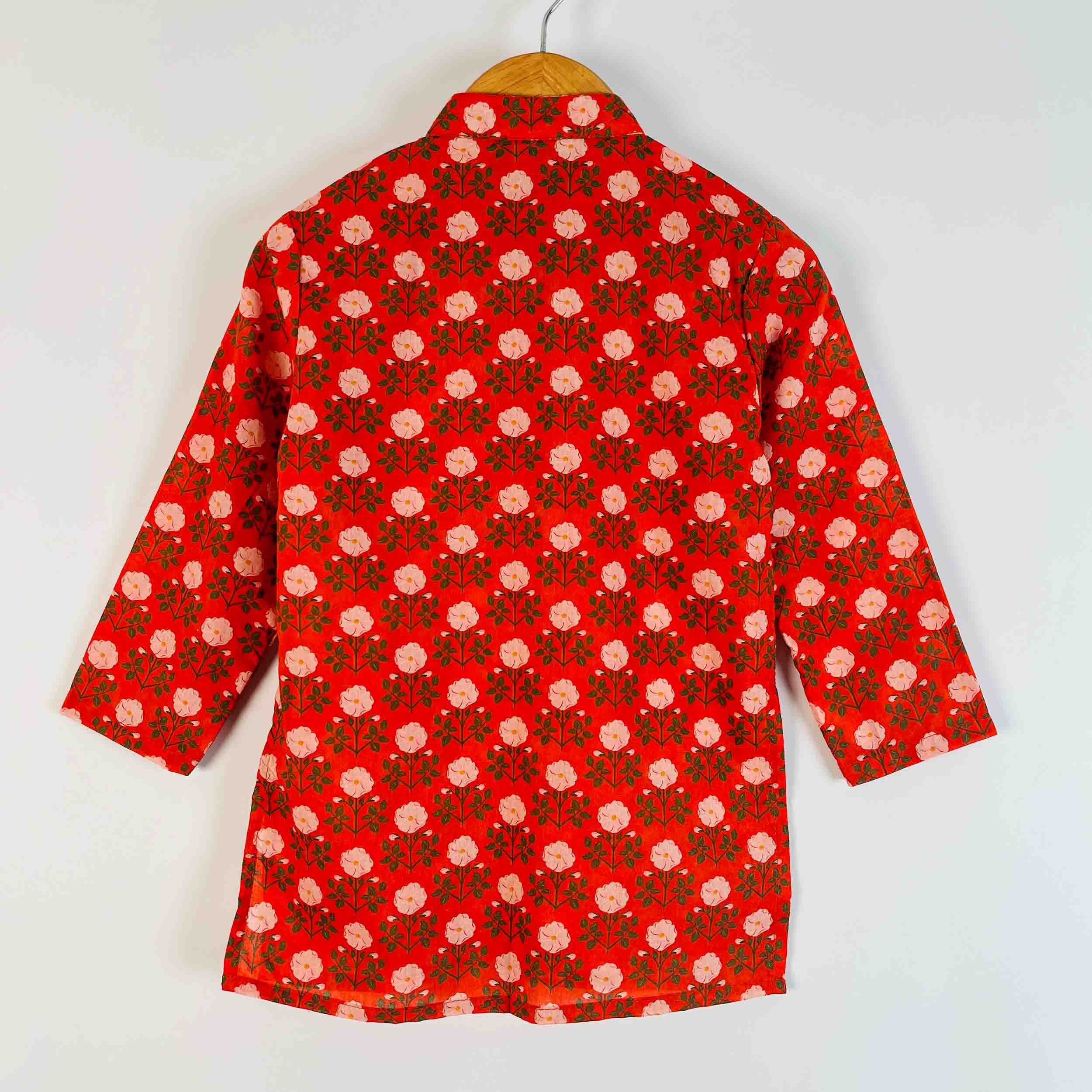 A red long-sleeve shirt with a repeating pink and green floral block print pattern, hanging on a wooden hanger against a plain white background.